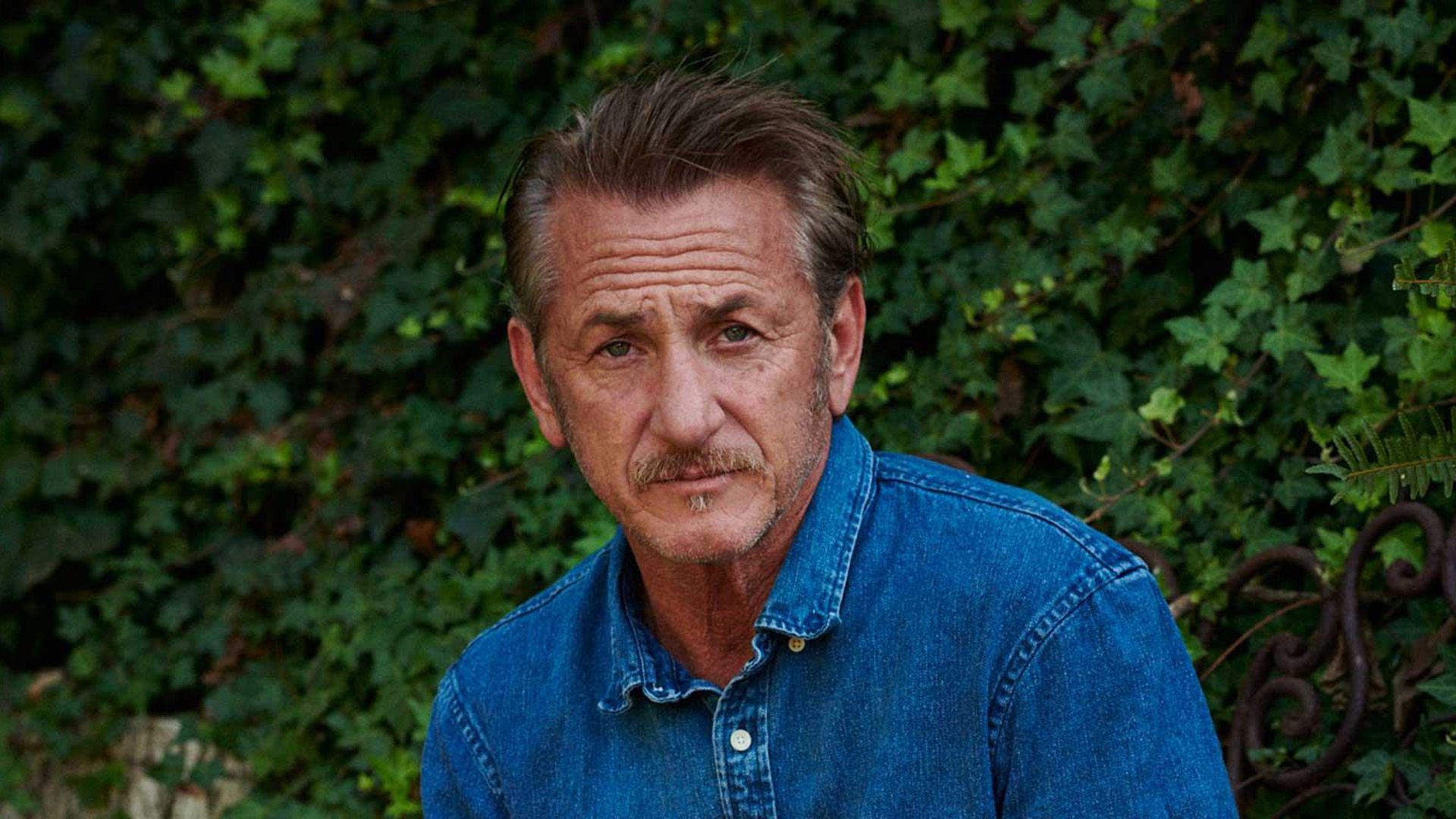 Sean Penn con una camicia di jeans su uno sfondo di edera verde
