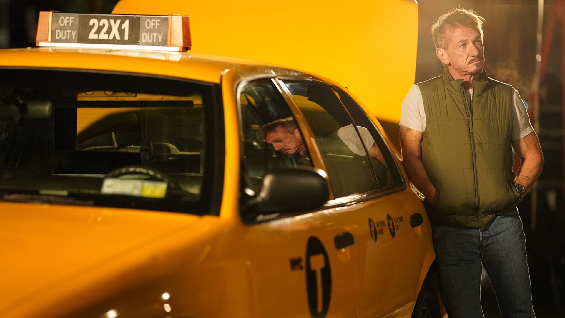 Sean Penn con un gilet verde appoggiato a un taxi giallo
