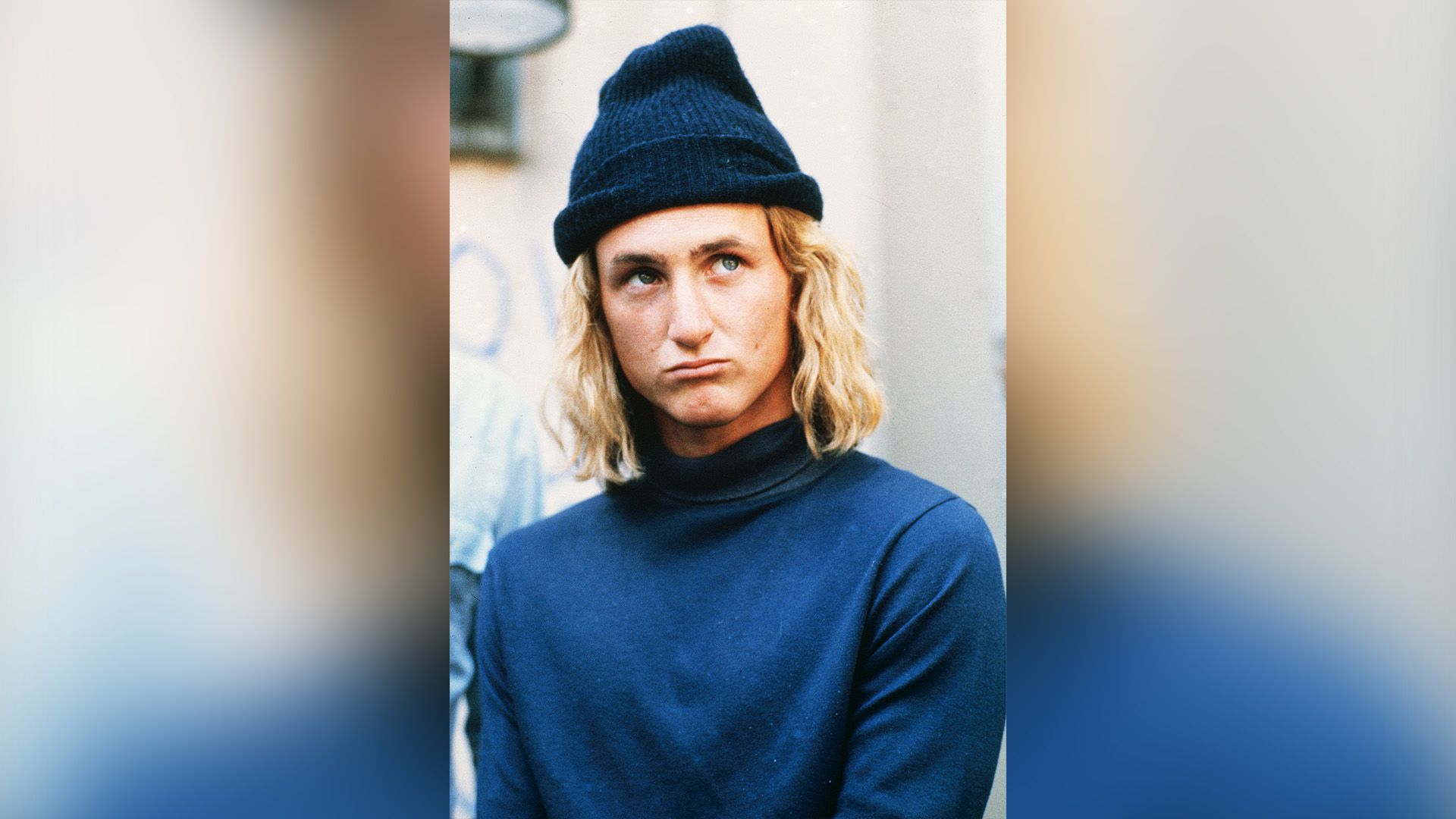 Il giovane Sean Penn con i capelli lunghi, indossa un dolcevita blu e un berretto blu
