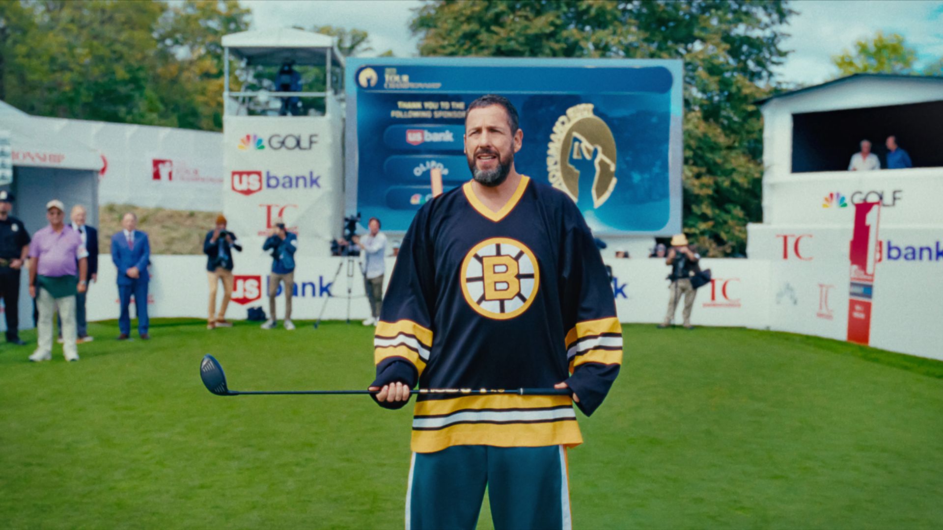 Adam Sandler con una maglia tiene una mazza da hockey mentre si trova in uno stadio