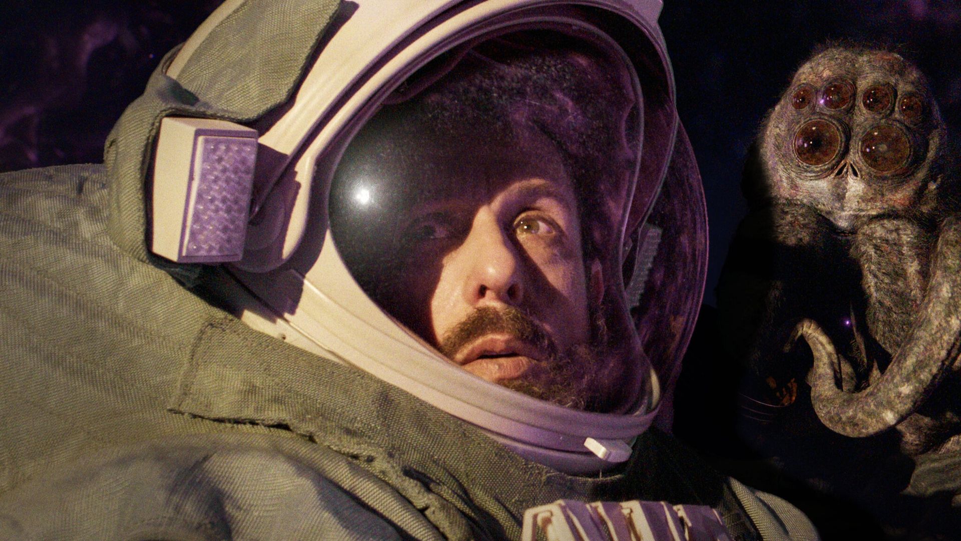 Adam Sandler con un casco da astronauta, con un insetto gigante sulla destra