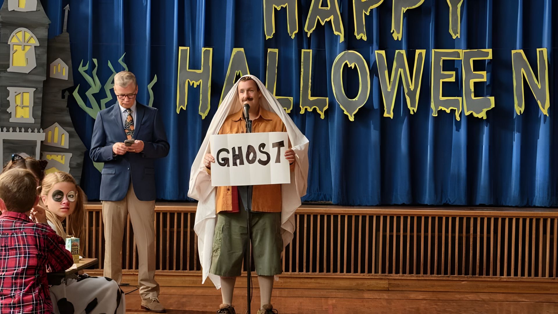 Adam Sandler con un lenzuolo in testa, tiene un cartello con scritto GHOST