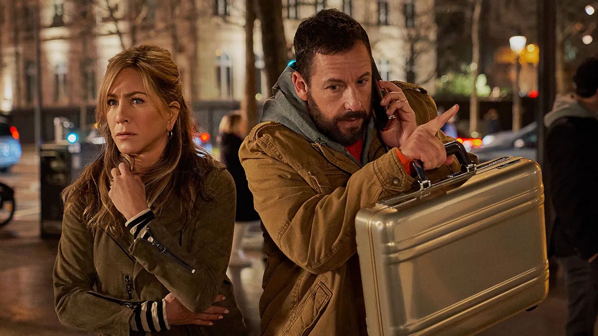 Jennifer Aniston e Adam Sandler per strada, lei sembra spaventata, lui parla al telefono e tiene una valigetta