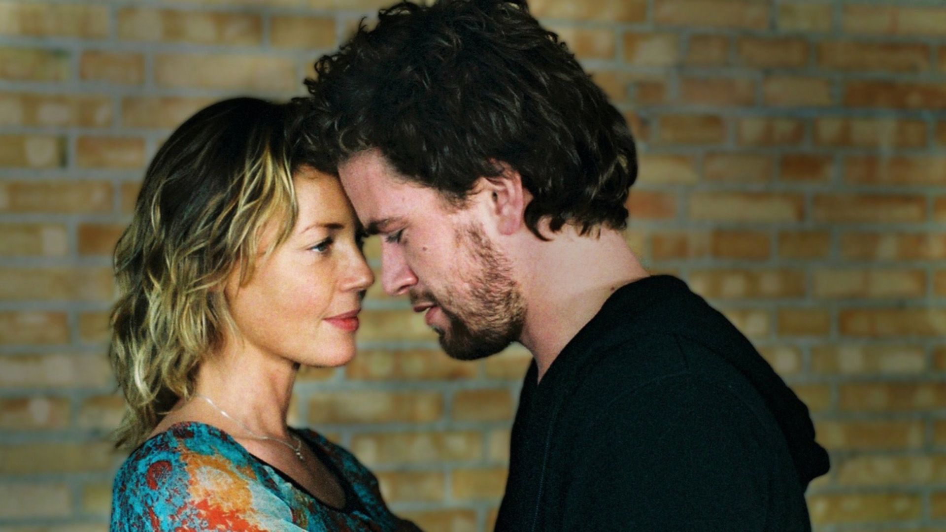Connie Nielsen e un uomo dai capelli scuri premono le loro fronti insieme