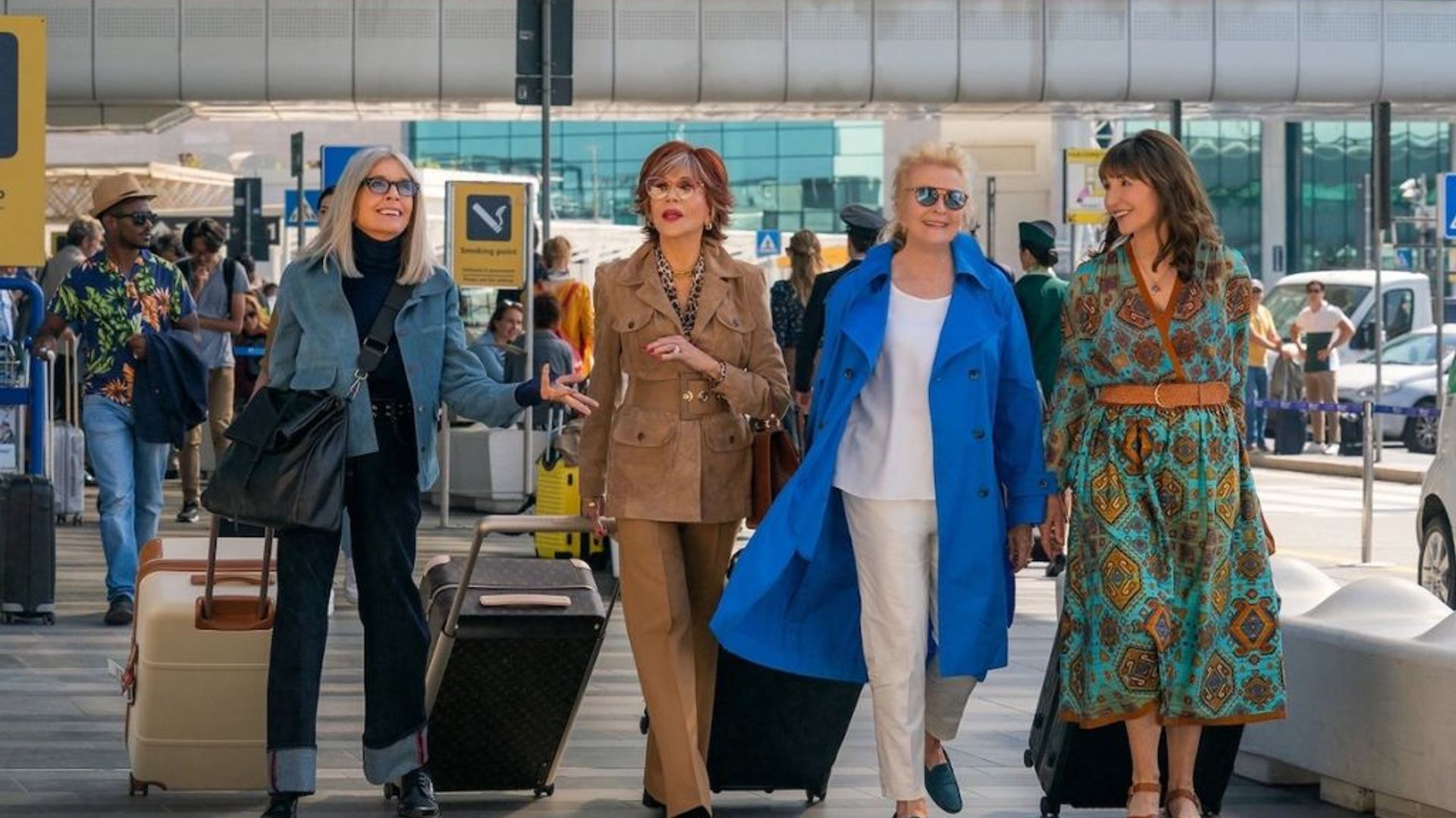Quattro donne eleganti di una certa età che camminano in aeroporto con i bagagli