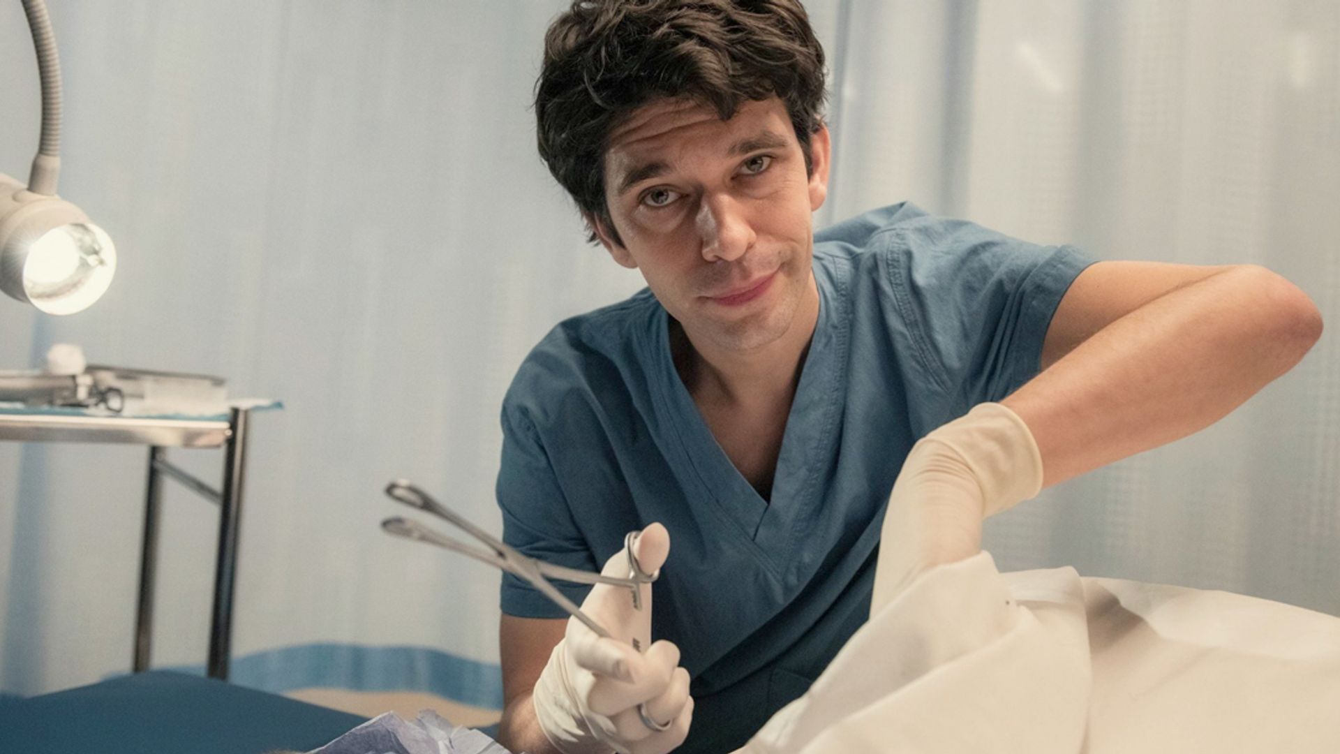 Ben Whishaw in camice da medico mentre tiene uno strumento medico, scena della serie This Is Going to Hurt