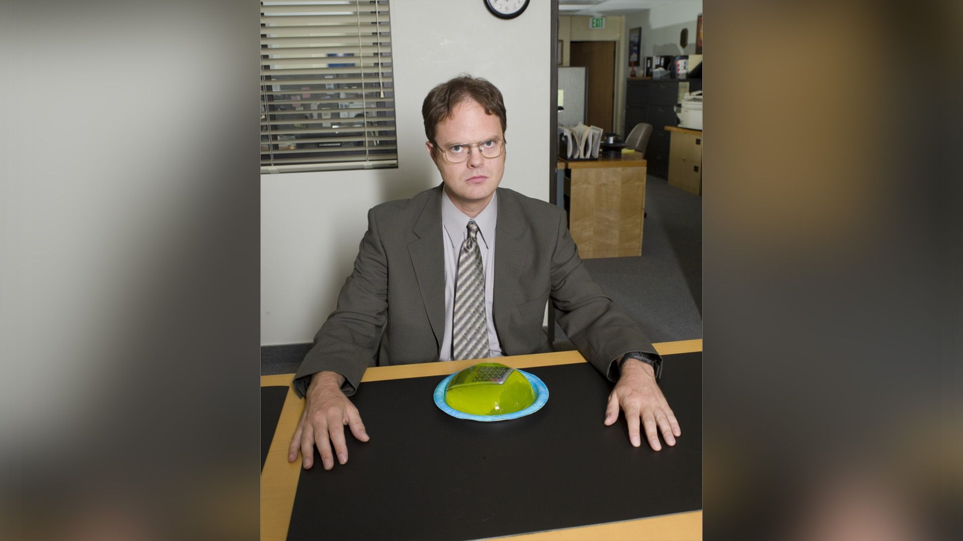 Rainn Wilson seduto a un tavolo con davanti un piatto contenente una calcolatrice ricoperta di gelatina verde