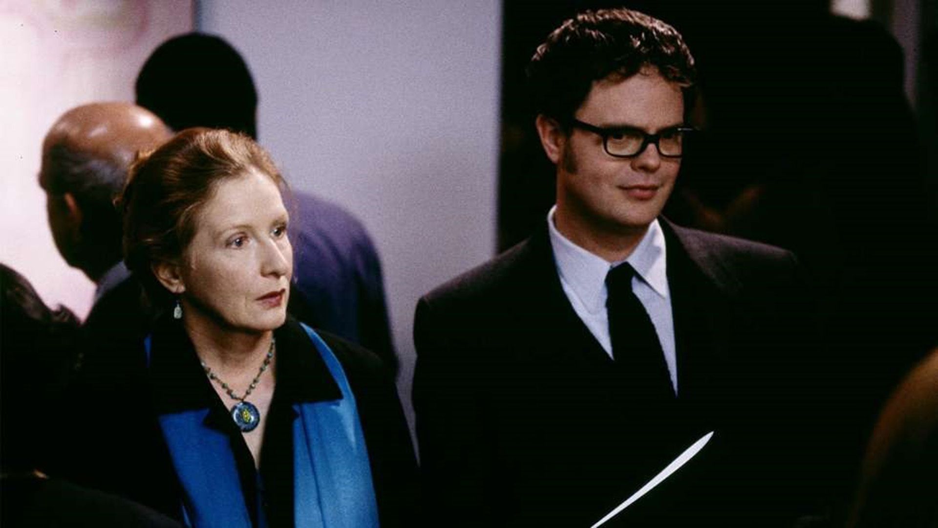 Rainn Wilson con occhiali e blazer, in piedi accanto a Frances Conroy con una sciarpa blu