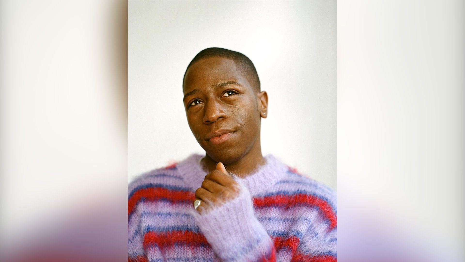 David Jonsson in un maglione soffice a righe rosse e viola guarda sognante verso l'alto