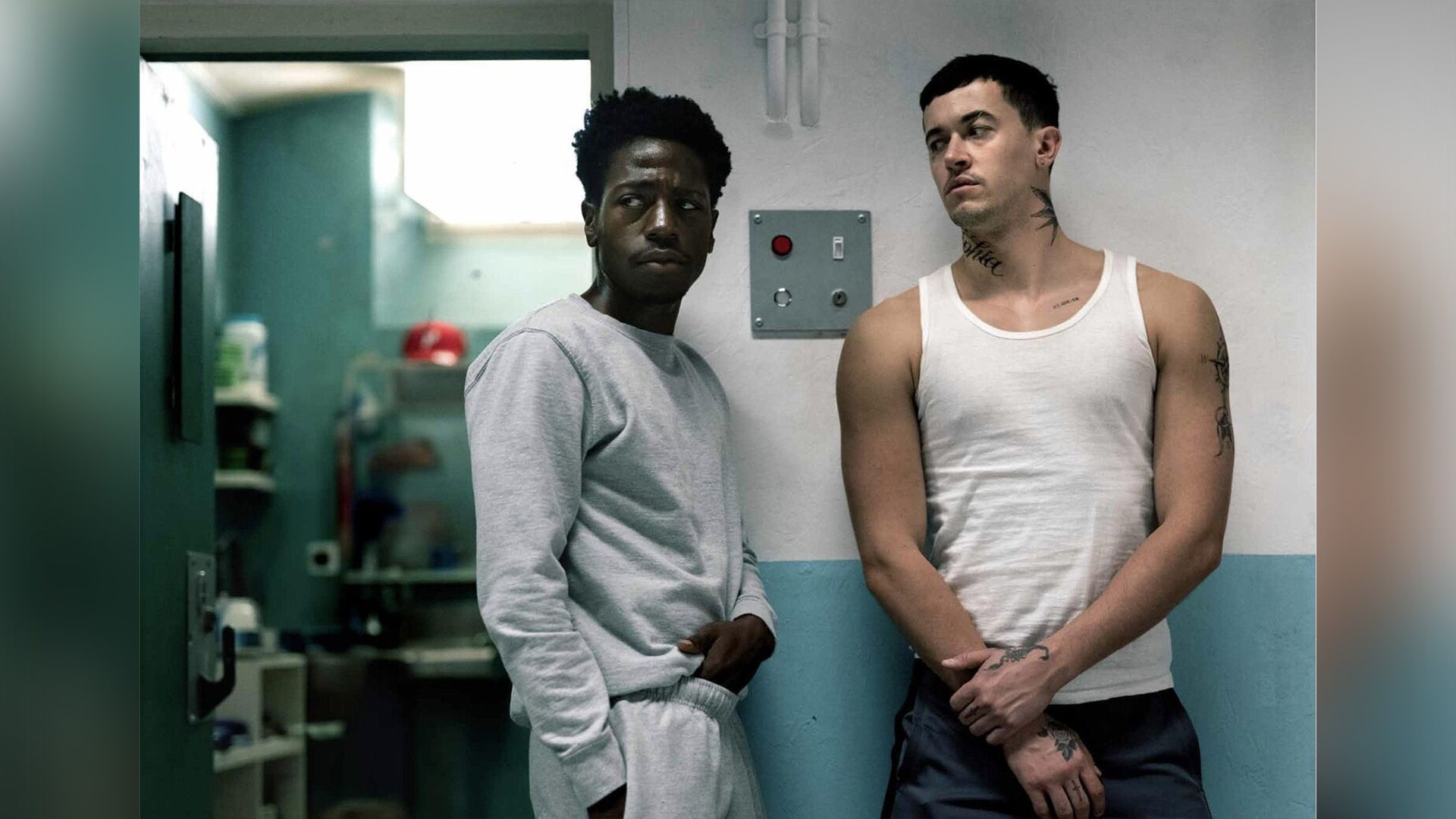 David Jonsson in tuta grigia in piedi accanto a una cella carceraria insieme a un uomo alto con canottiera bianca