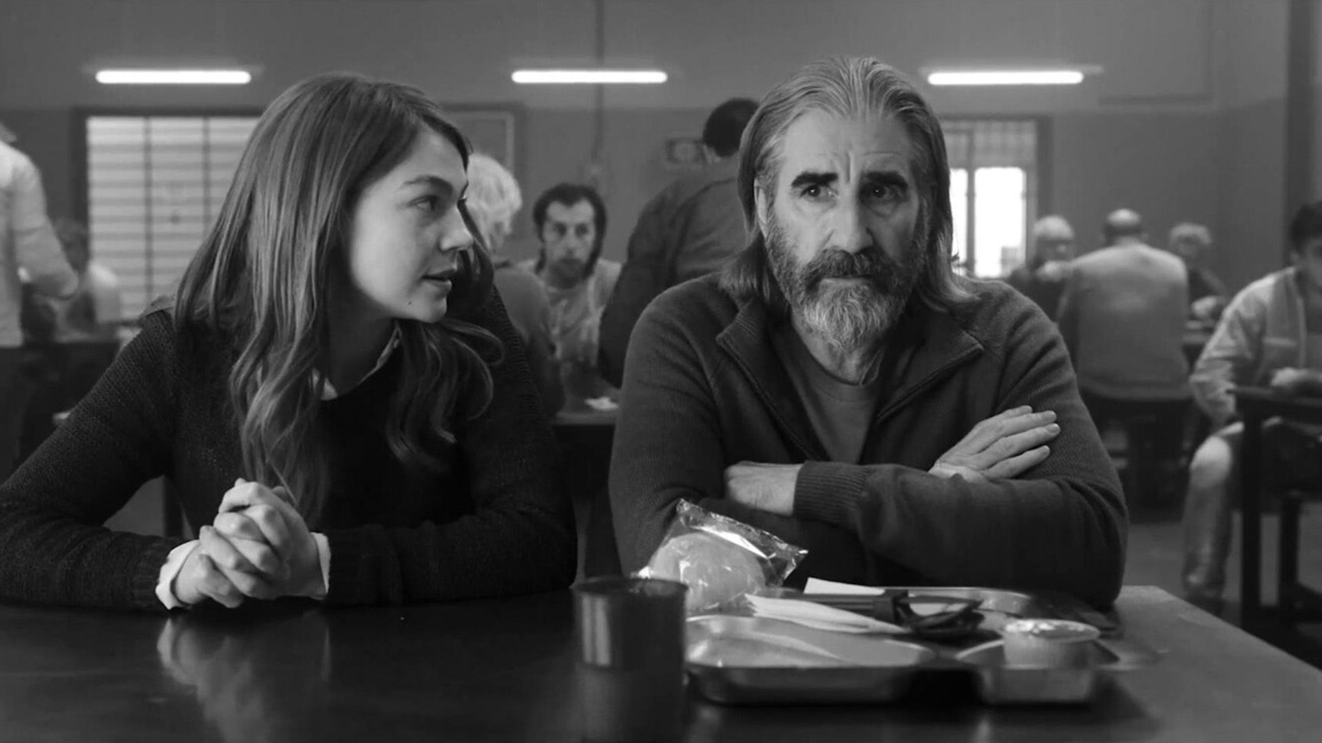 John Lynch seduto a un tavolo nella sala da pranzo, una ragazza seduta accanto a lui che dice qualcosa