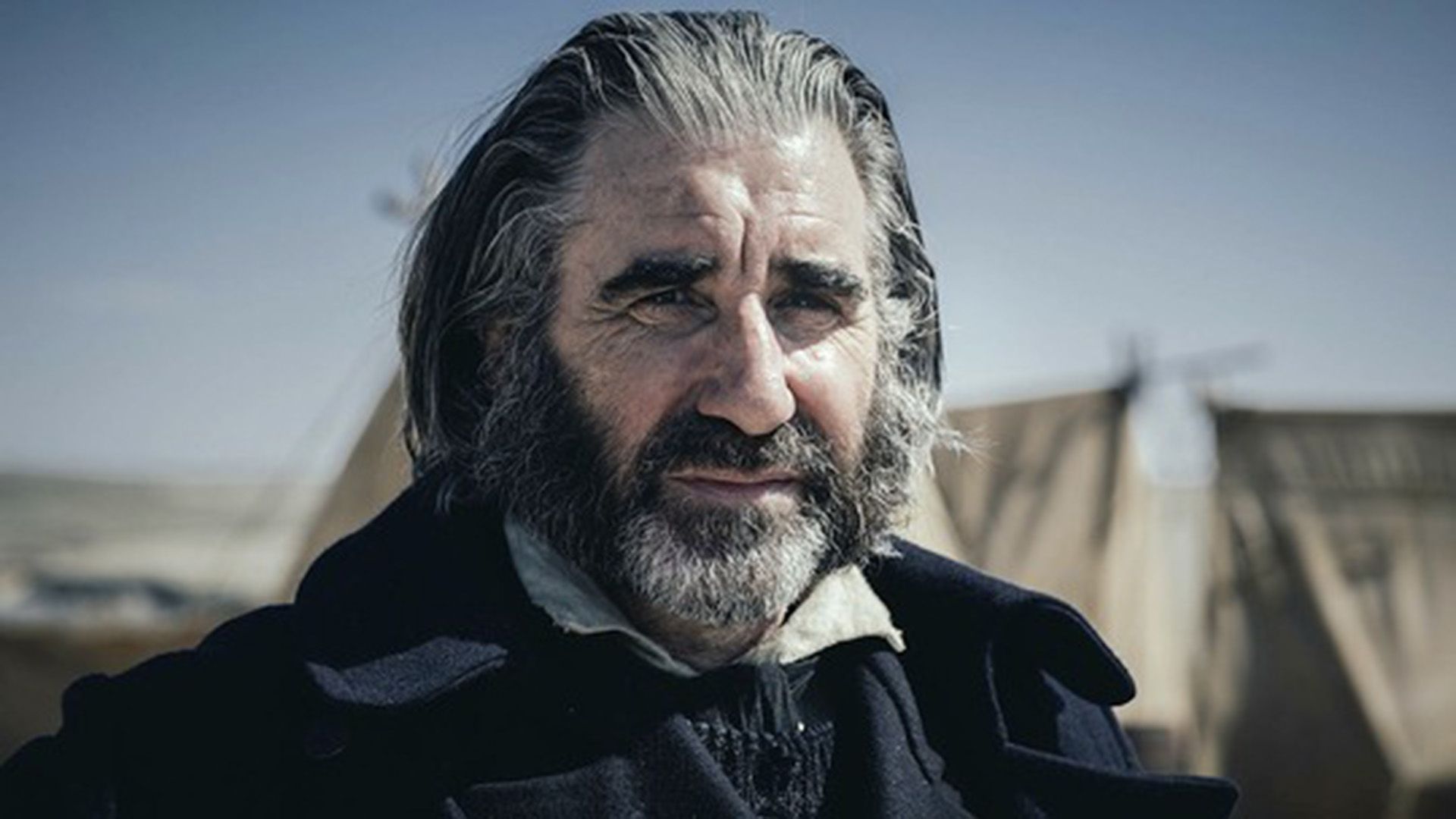 John Lynch con la barba grigia strizza gli occhi alla luce del sole