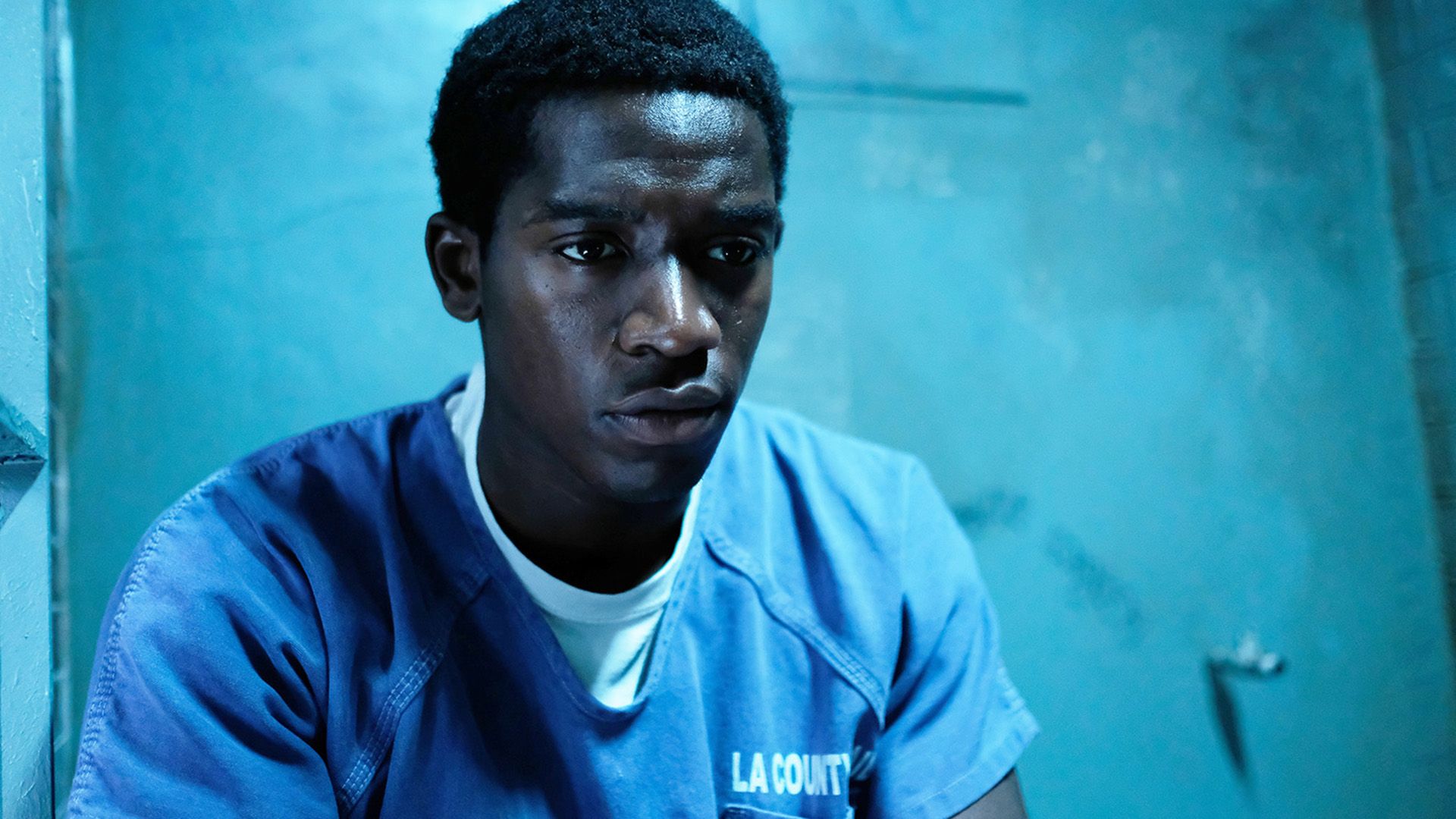 Damson Idris in una camicia da prigione blu seduto in una cella