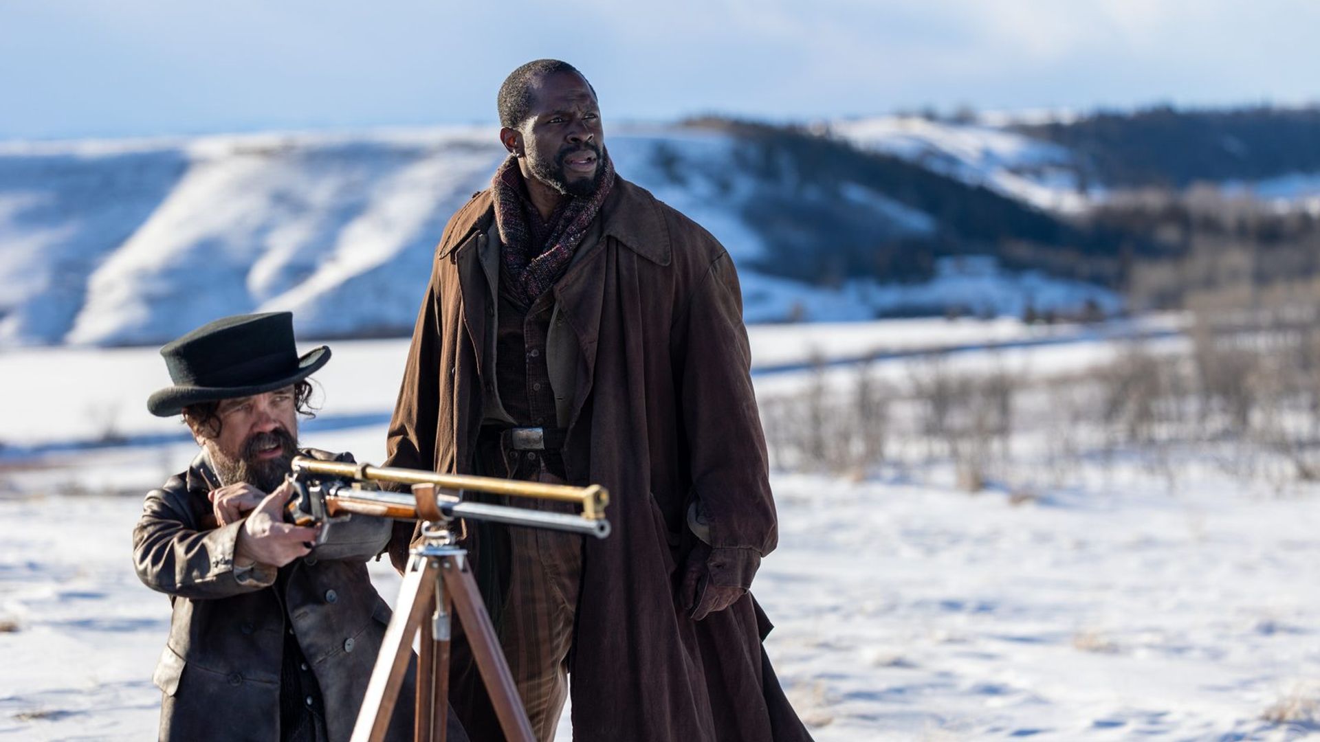 Peter Dinklage e Gbenga Akinnagbe in piedi nella neve, uno punta un fucile montato su un treppiede, l'altro guarda in lontananza