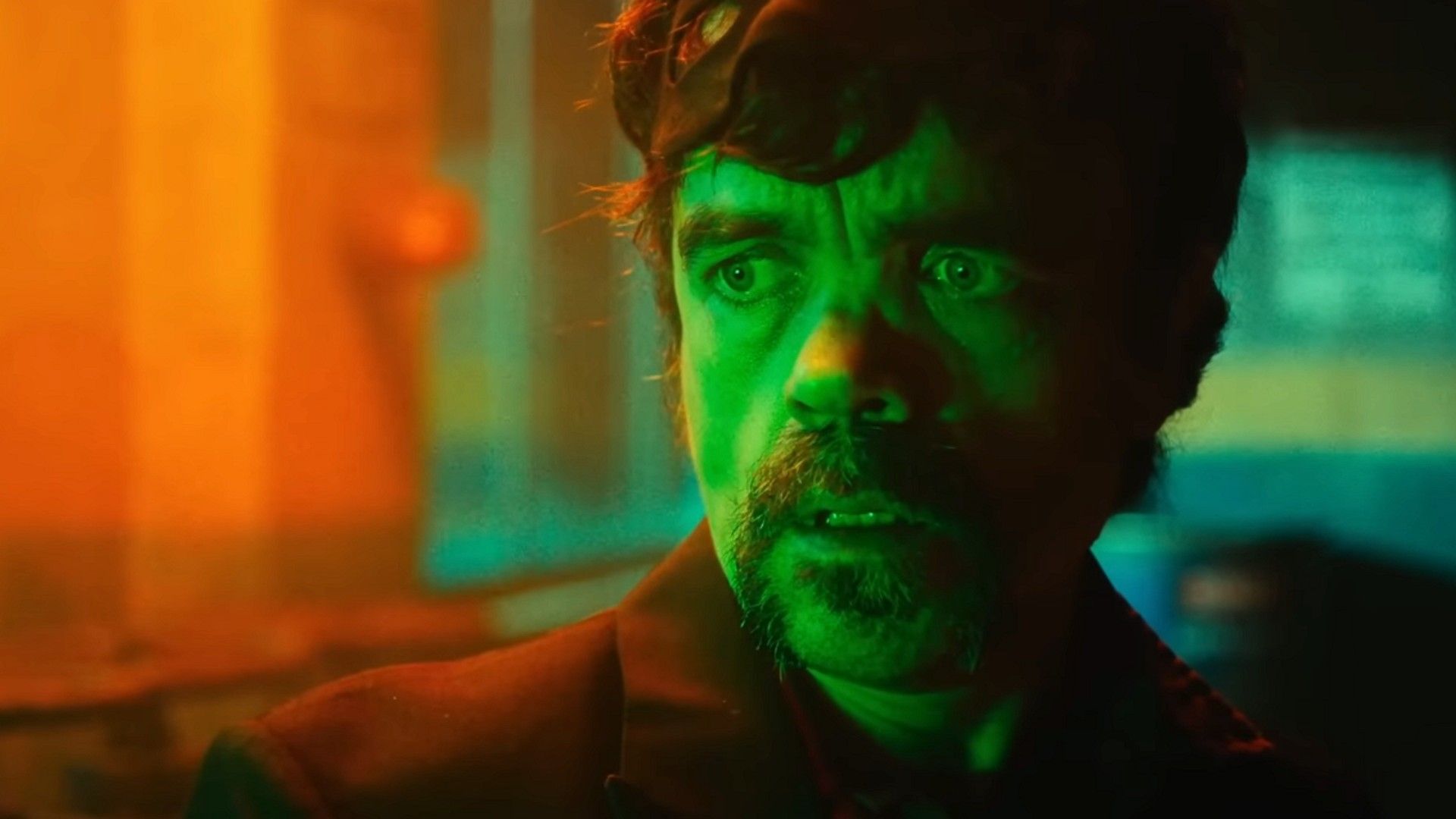 Peter Dinklage in piedi in una stanza buia illuminata da luce verde e arancione