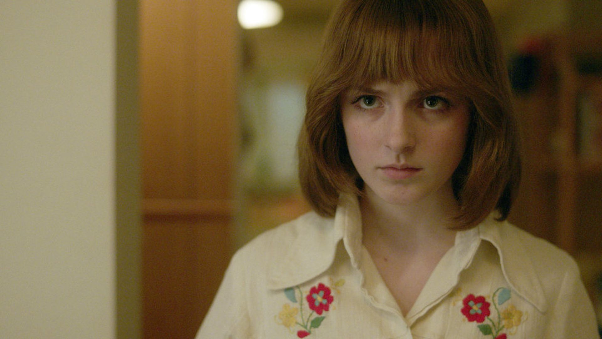 Mckenna Grace con caschetto rosso e moda anni '80, scena della miniserie