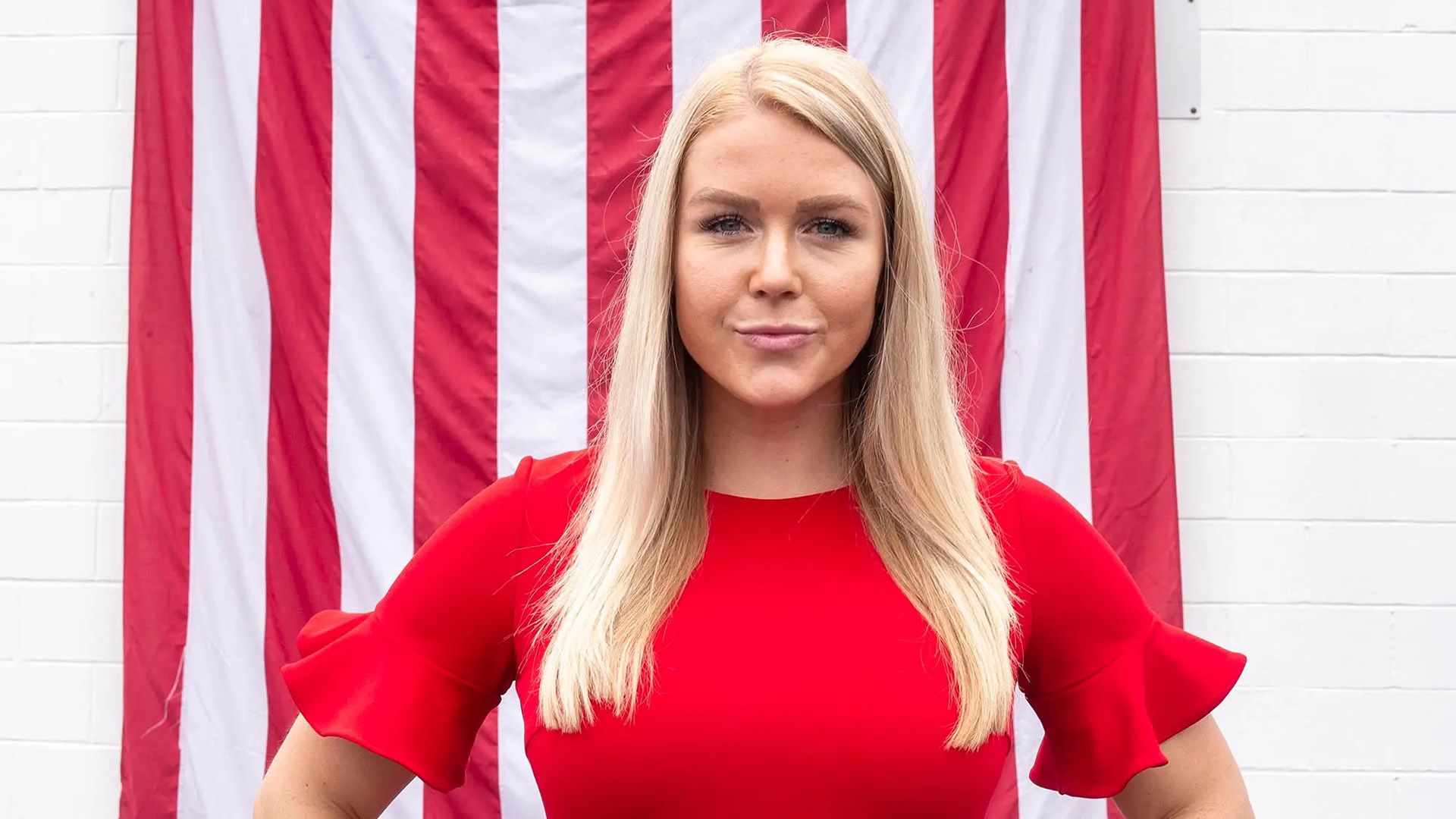 Una bionda dai capelli lunghi in un vestito rosso di fronte alla bandiera americana