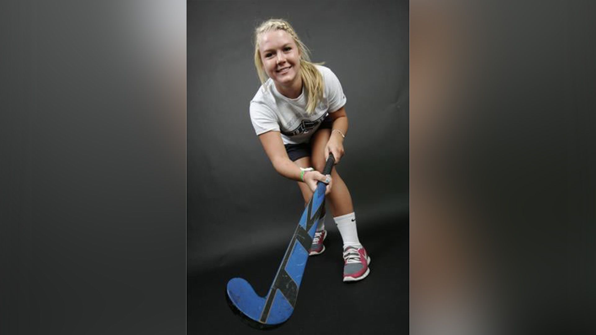 Una giovane ragazza sorridente con un bastone da hockey su sfondo nero