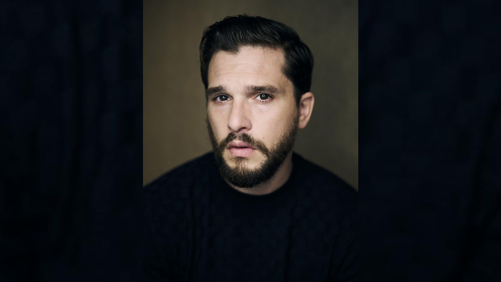 Ritratto dell'attore Kit Harington: indossa una maglietta nera, taglio di capelli alla moda, barba curata