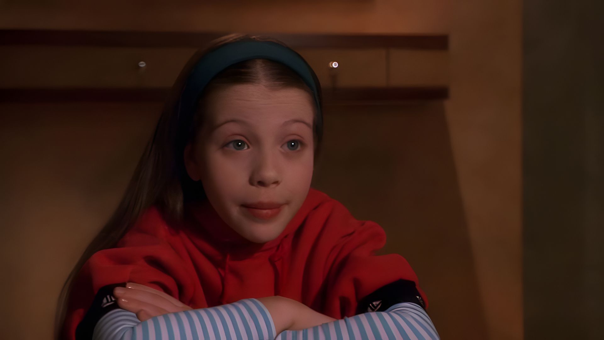 L'attrice Michelle Trachtenberg da bambina, con un maglione rosso, scaldamuscoli a righe e una fascia verde