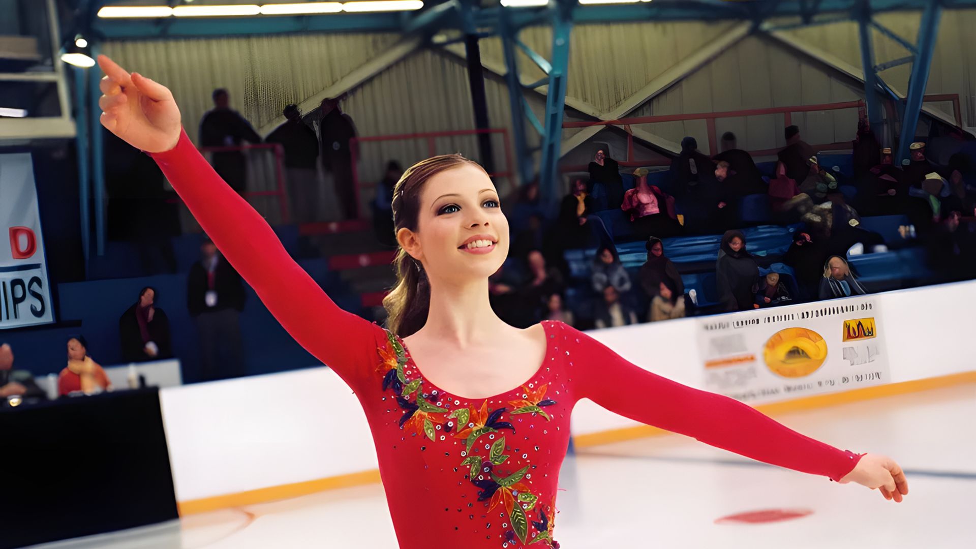Michelle Trachtenberg in un costume da pattinatrice rosso danza sul ghiaccio, braccia sollevate