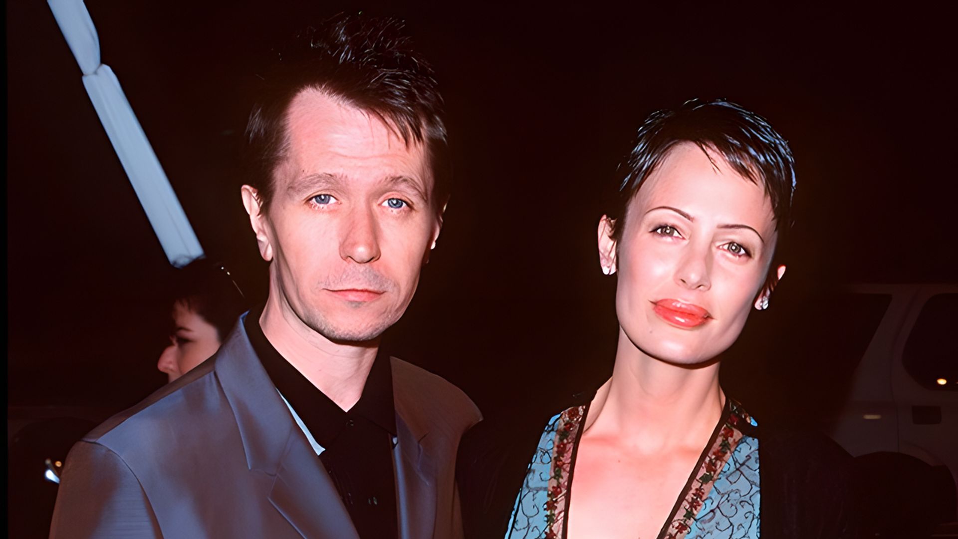 Gary Oldman in completo scuro e Donya Fiorentino in un elegante abito posano insieme a un evento serale.