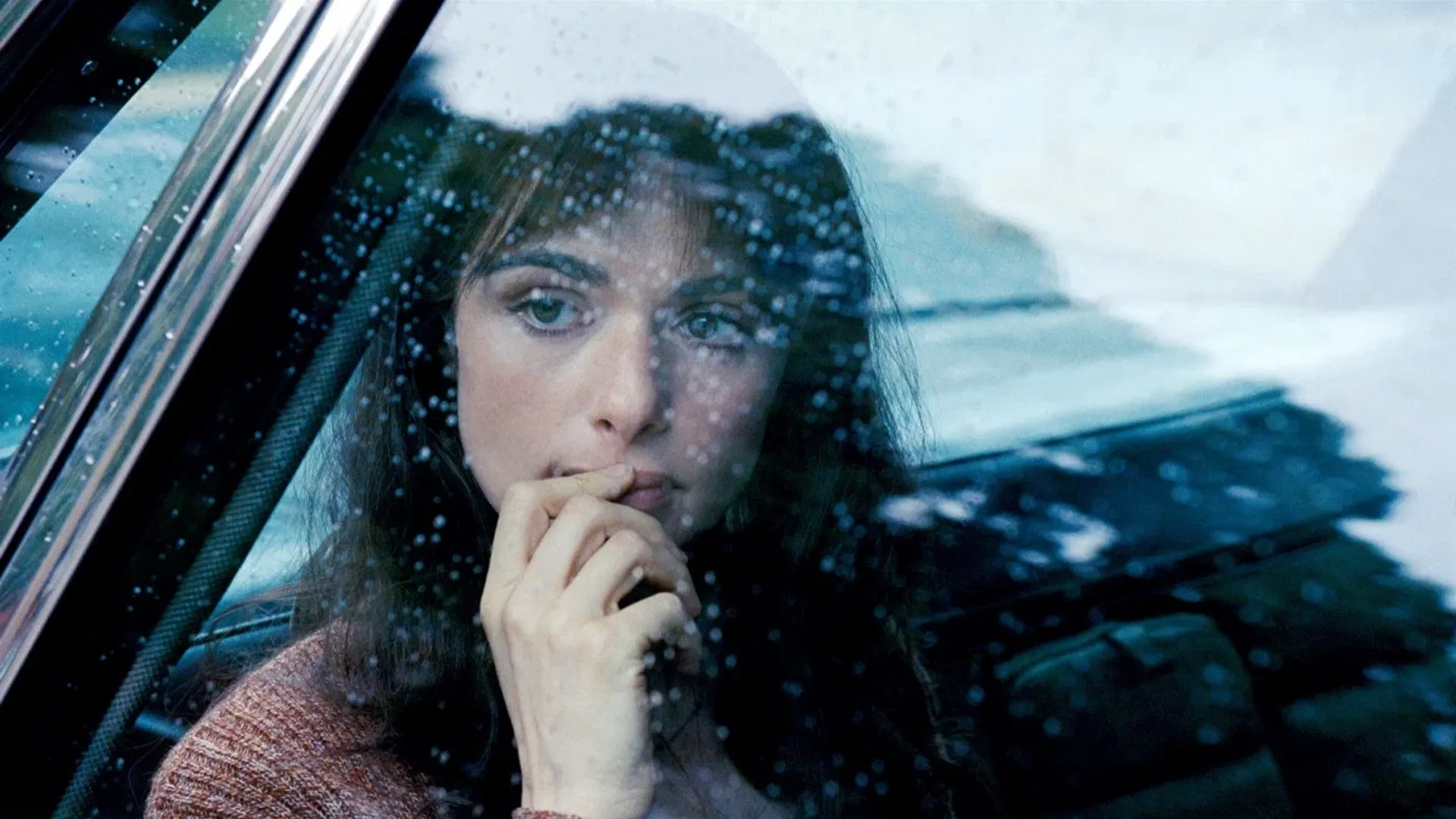 Primo piano del volto dell'attrice Rachel Weisz ripreso attraverso il vetro di un'auto sotto la pioggia