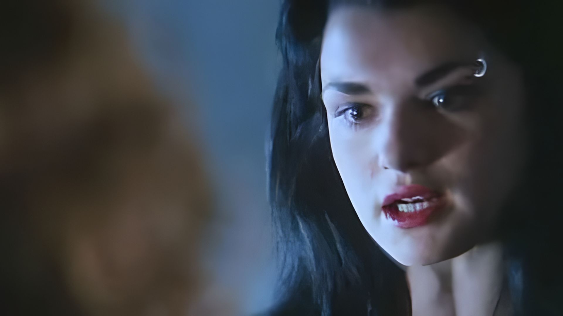 Un primo piano del volto di Rachel Weisz, ha un rossetto rosso acceso e un anello al sopracciglio
