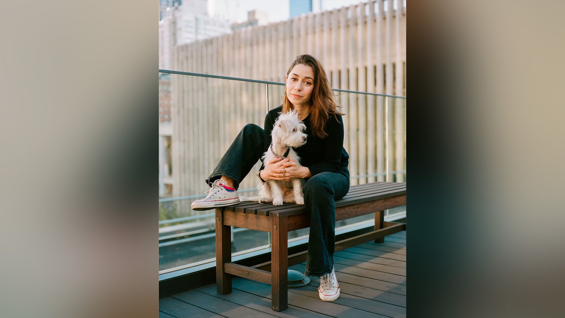 Cristin Milioti seduta su una panchina, abbracciando un piccolo cane bianco e soffice