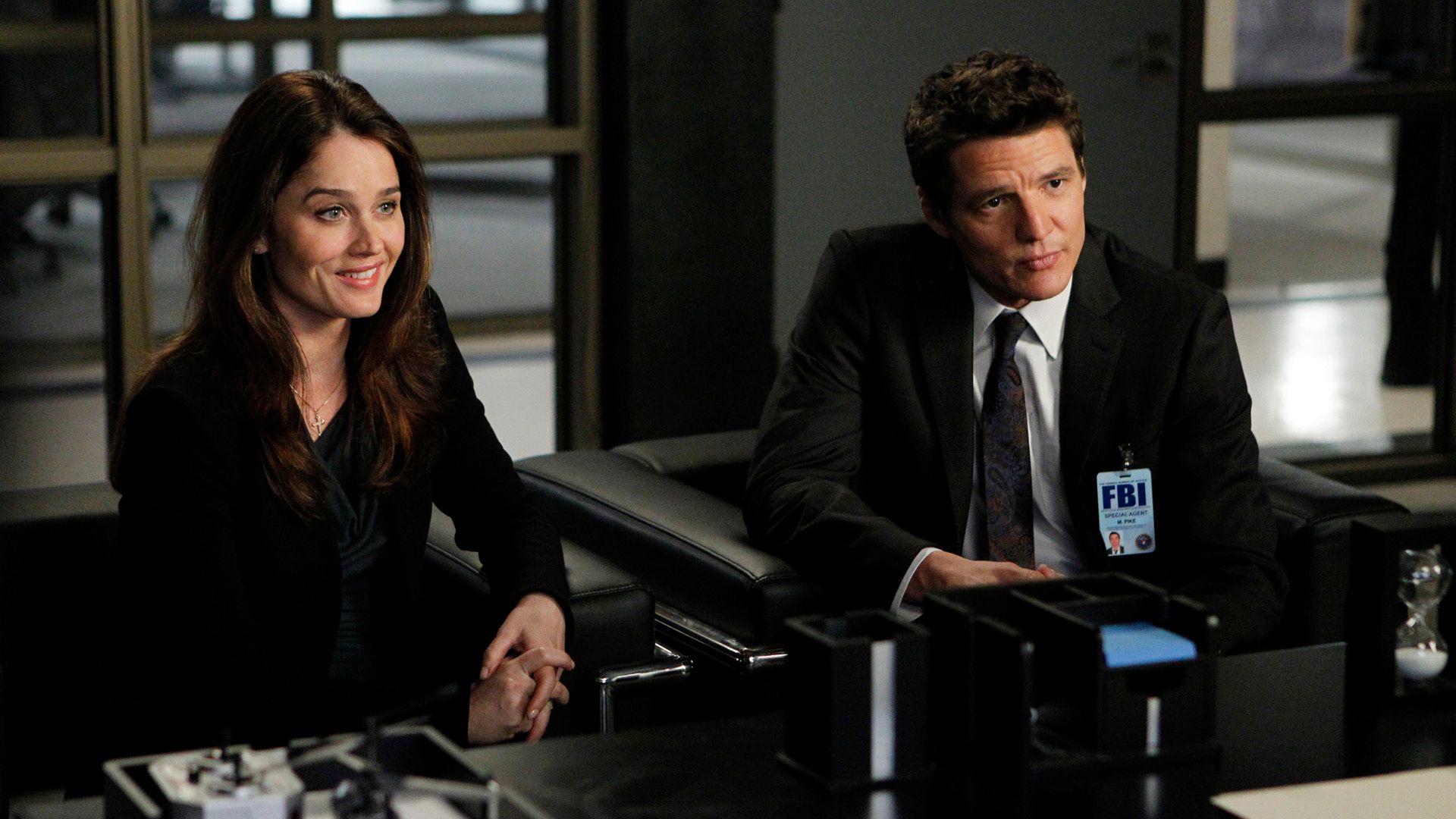 Pedro Pascal con un distintivo da agente FBI e Robin Tunney seduti a un tavolo nella serie "The Mentalist"