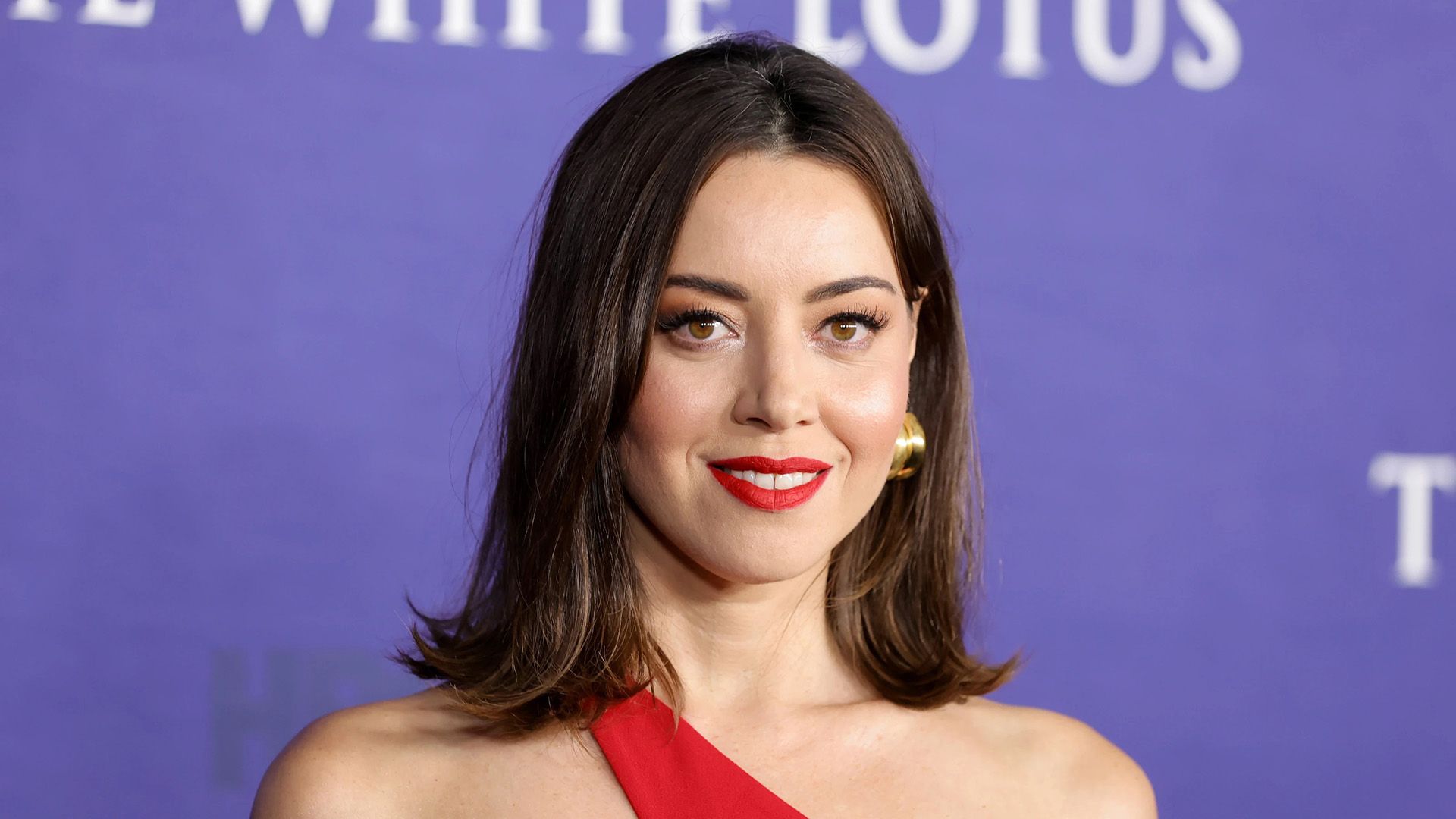 Attrice Aubrey Plaza in un vestito rosso su uno sfondo viola