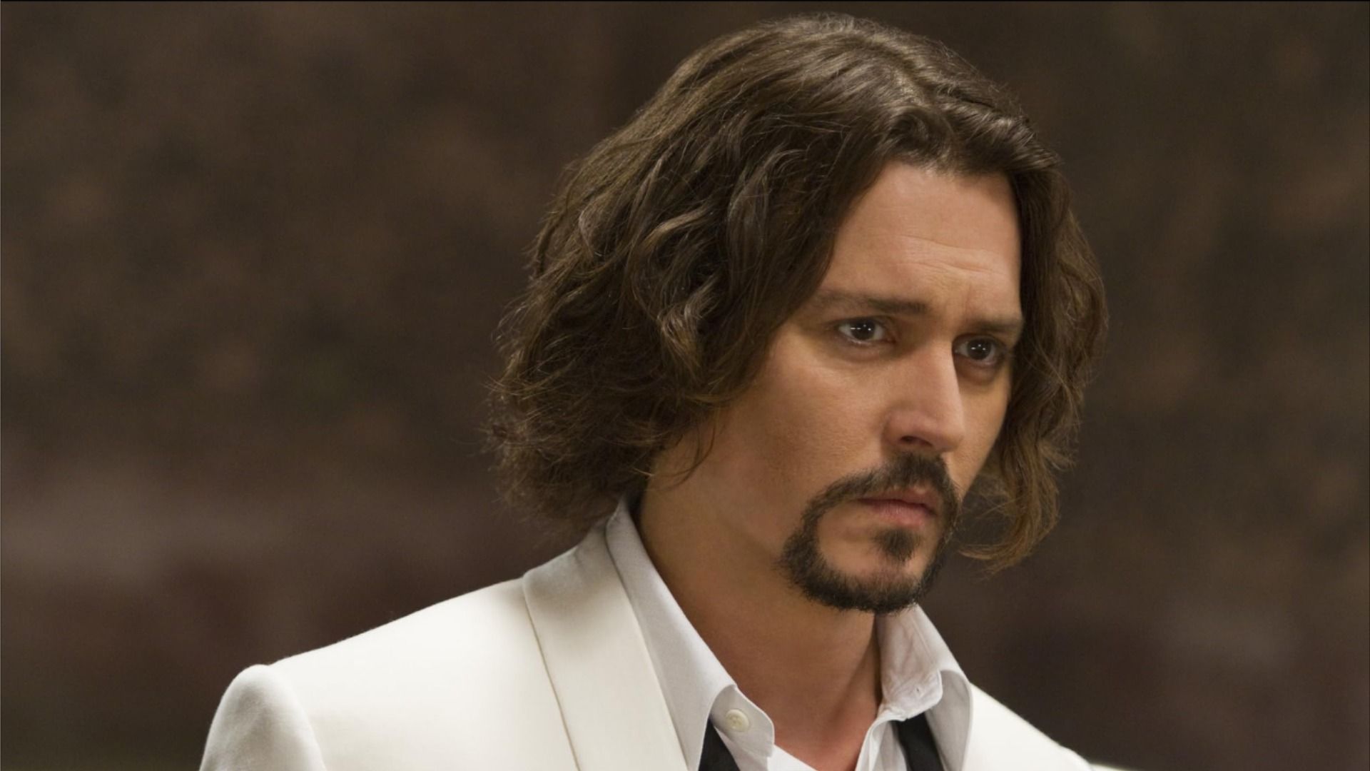 Attore Johnny Depp in giacca bianca e con i capelli lunghi guarda di lato