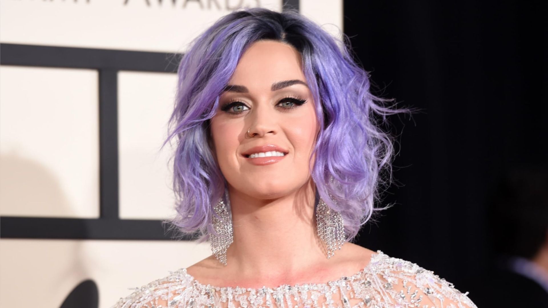 Singer Katy Perry in a sparkling dress smiles at the camera against a black-and-white background
