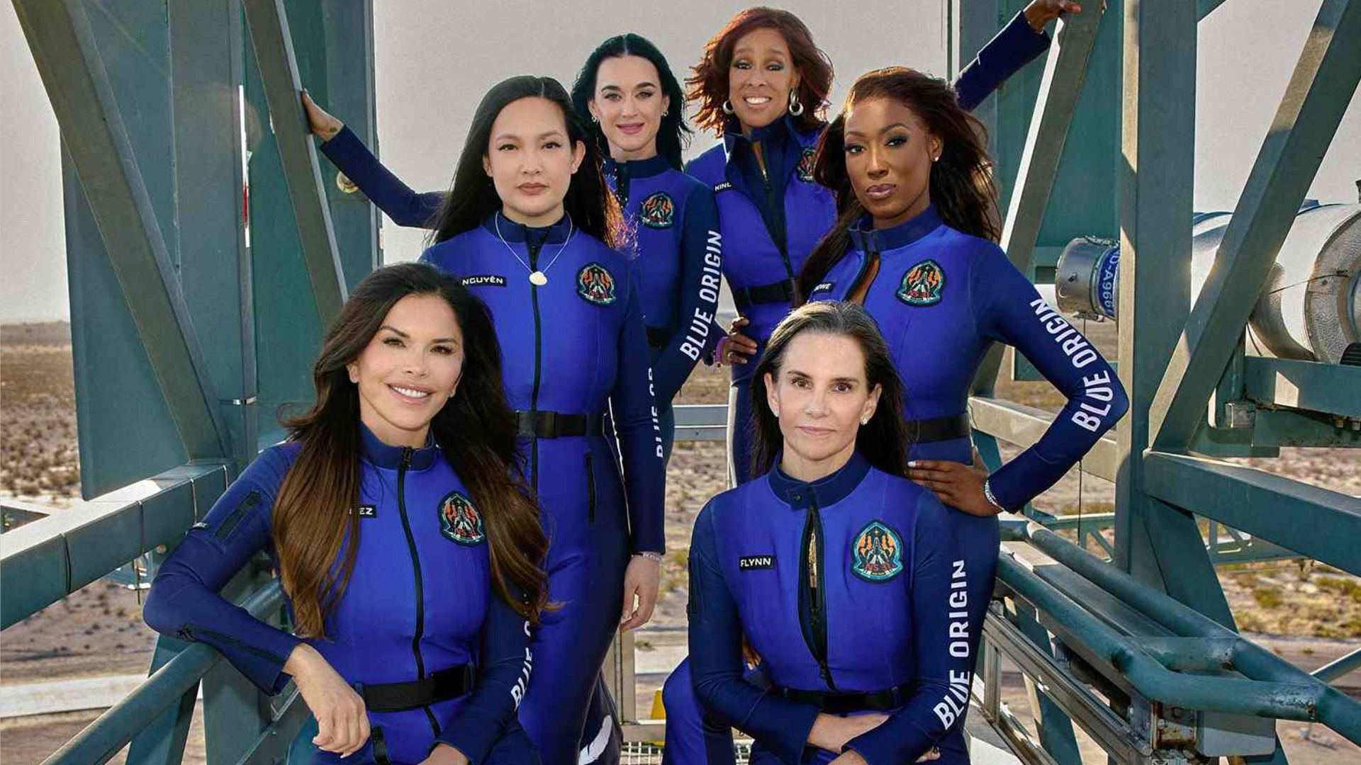Sei donne in tute spaziali blu posano e sorridono nell'ascensore