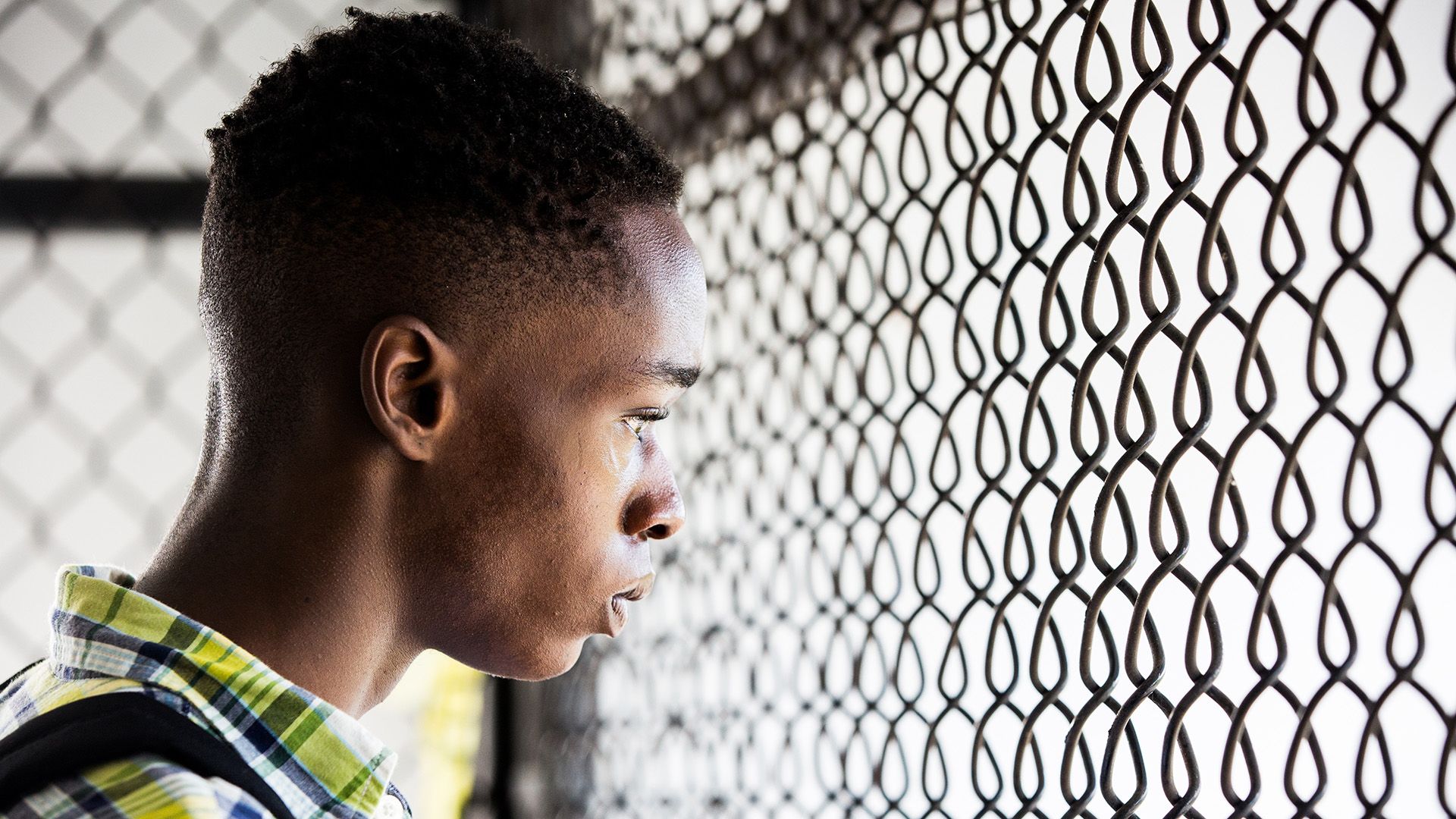 Ashton Sanders in una camicia a quadri guarda attraverso la rete di ferro