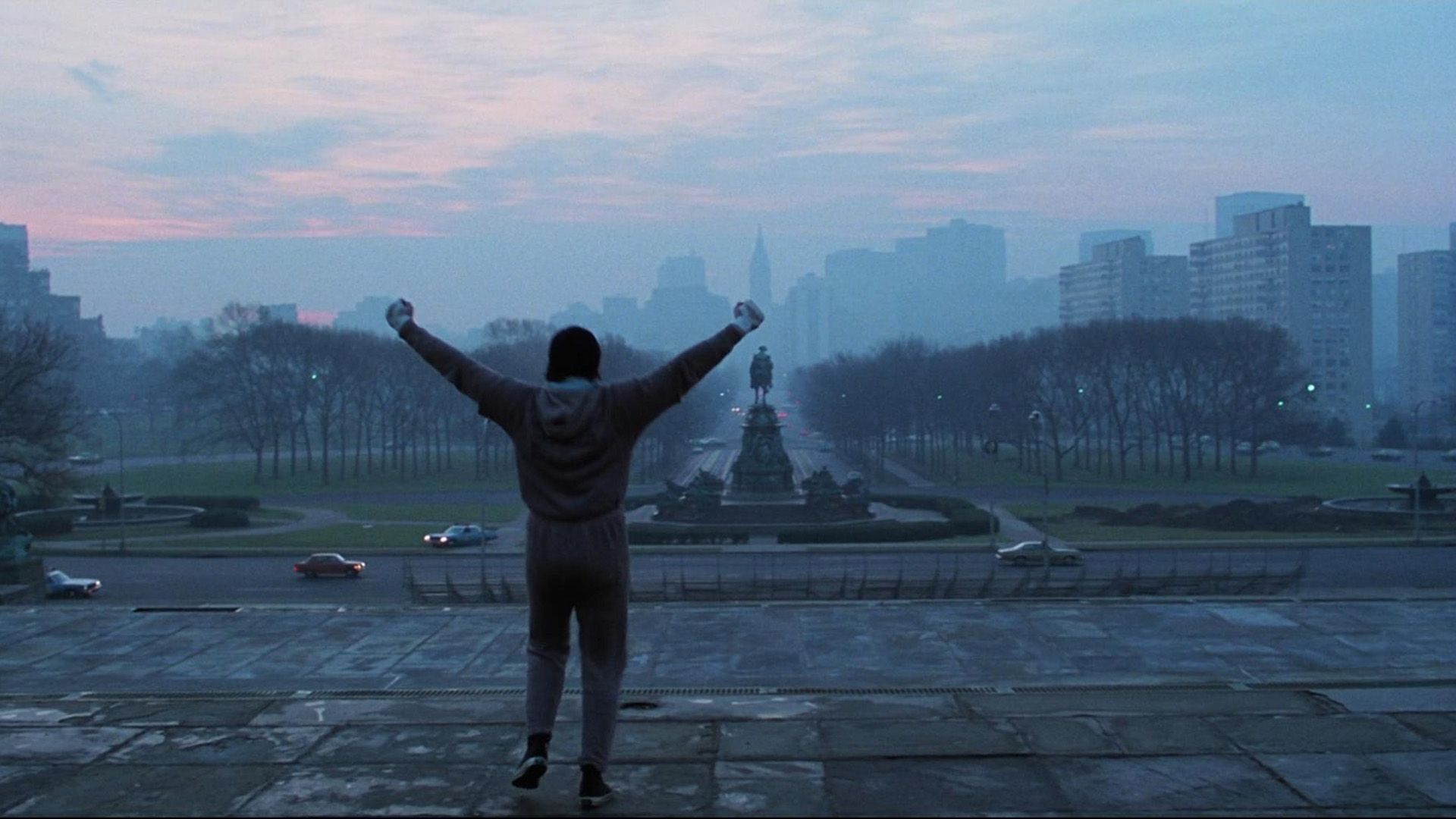 Un giovane Sylvester Stallone si trova nella piazza della città alzando le mani