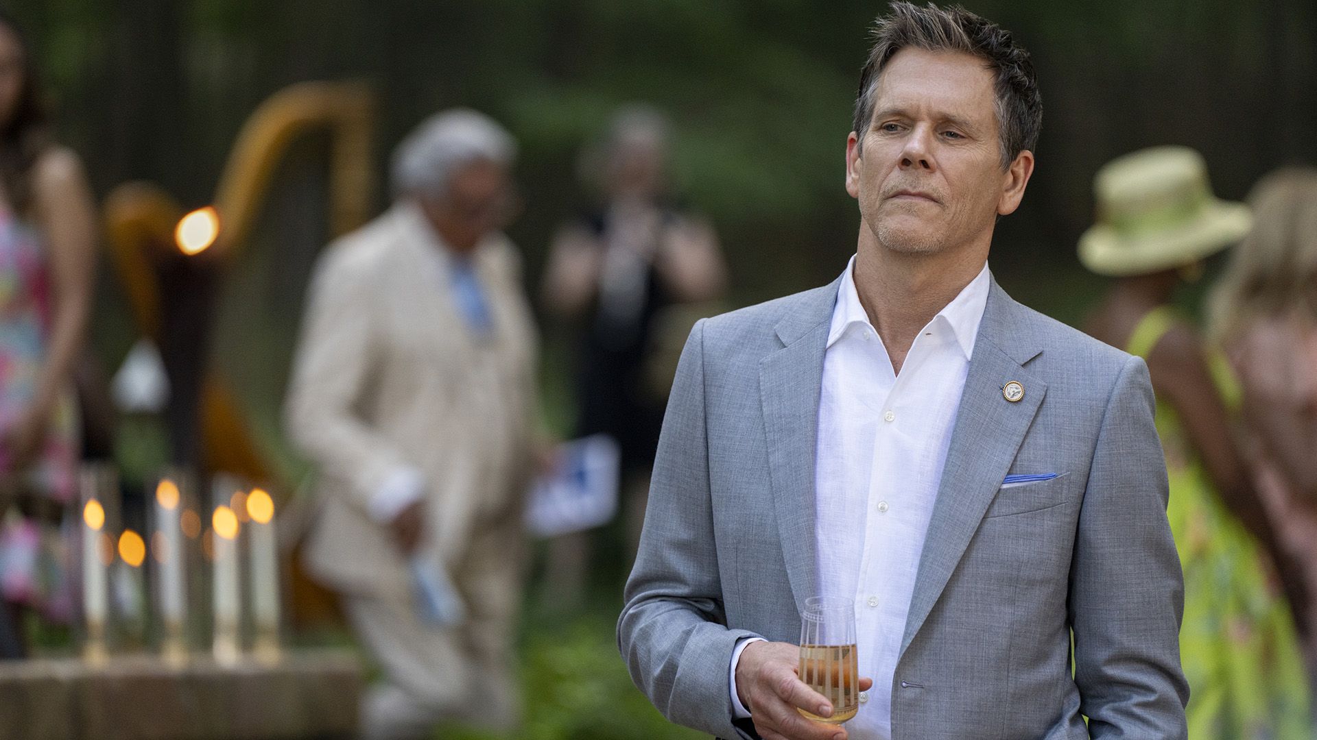 Attore Kevin Bacon in una giacca grigia e con in mano un bicchiere