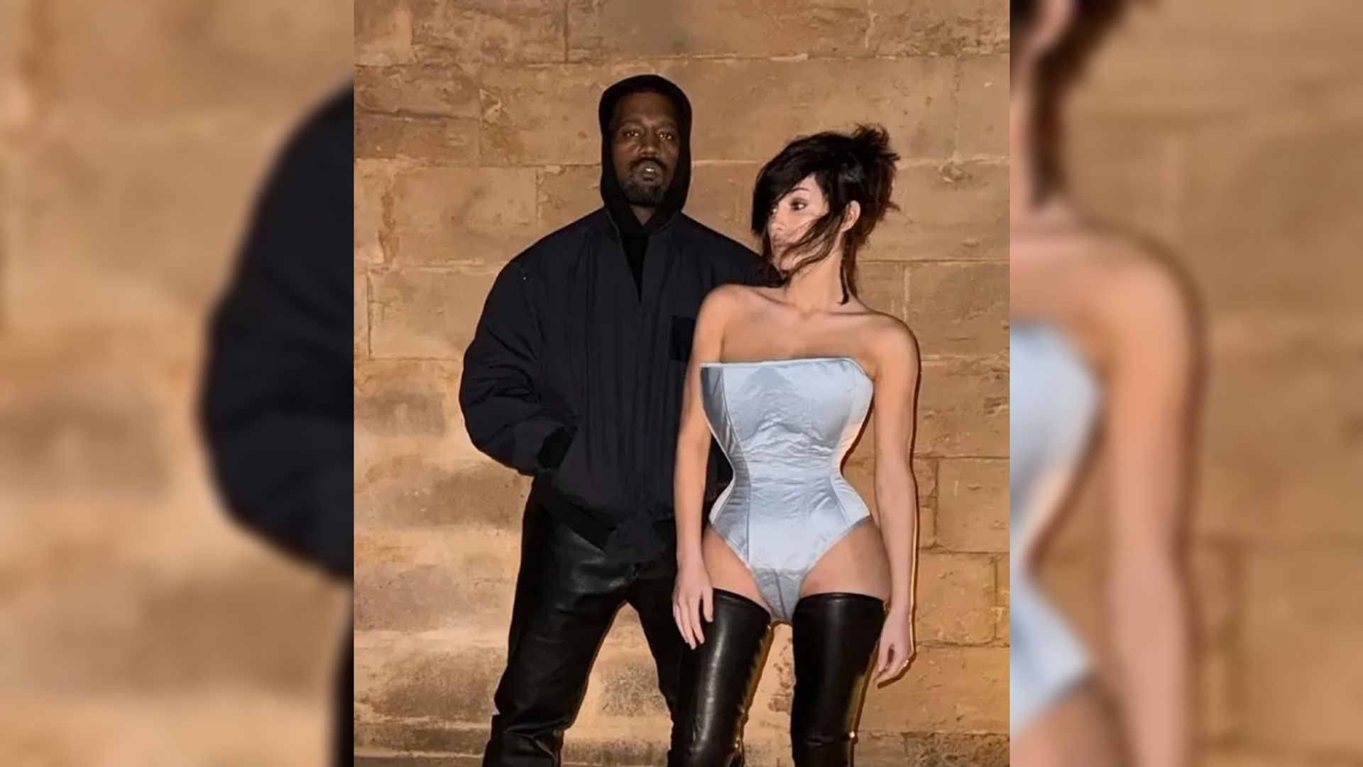 Il rapper Kanye West in un bomber nero e sua moglie Bianca Censori in un body blu posano contro un muro