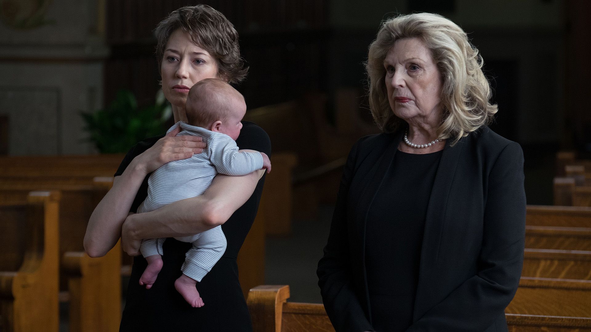 Carrie Coon con un bambino in braccio e un'anziana donna vestita di nero in piedi nella chiesa