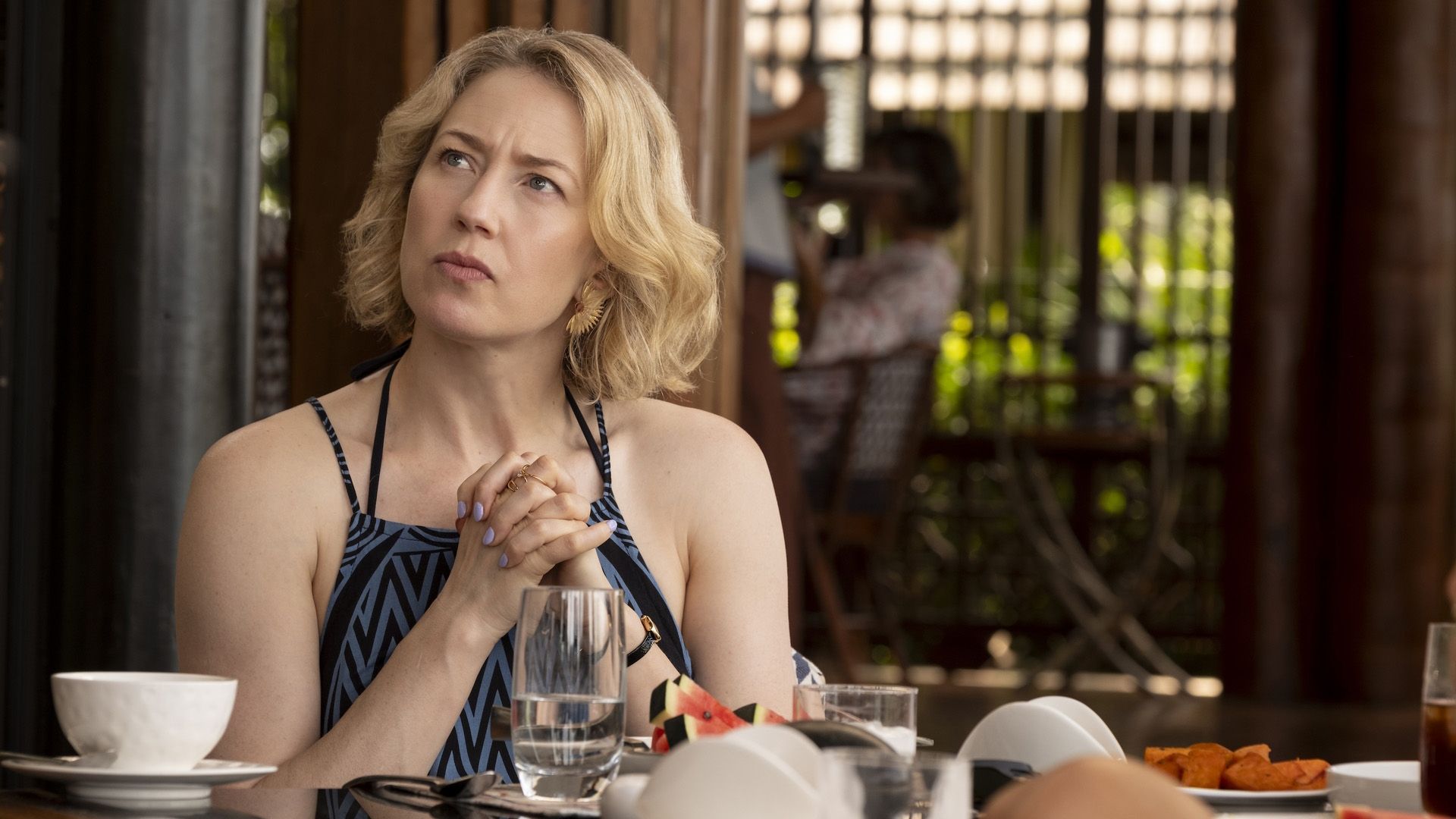 Carrie Coon in un vestito estivo seduta a un tavolo di un caffè