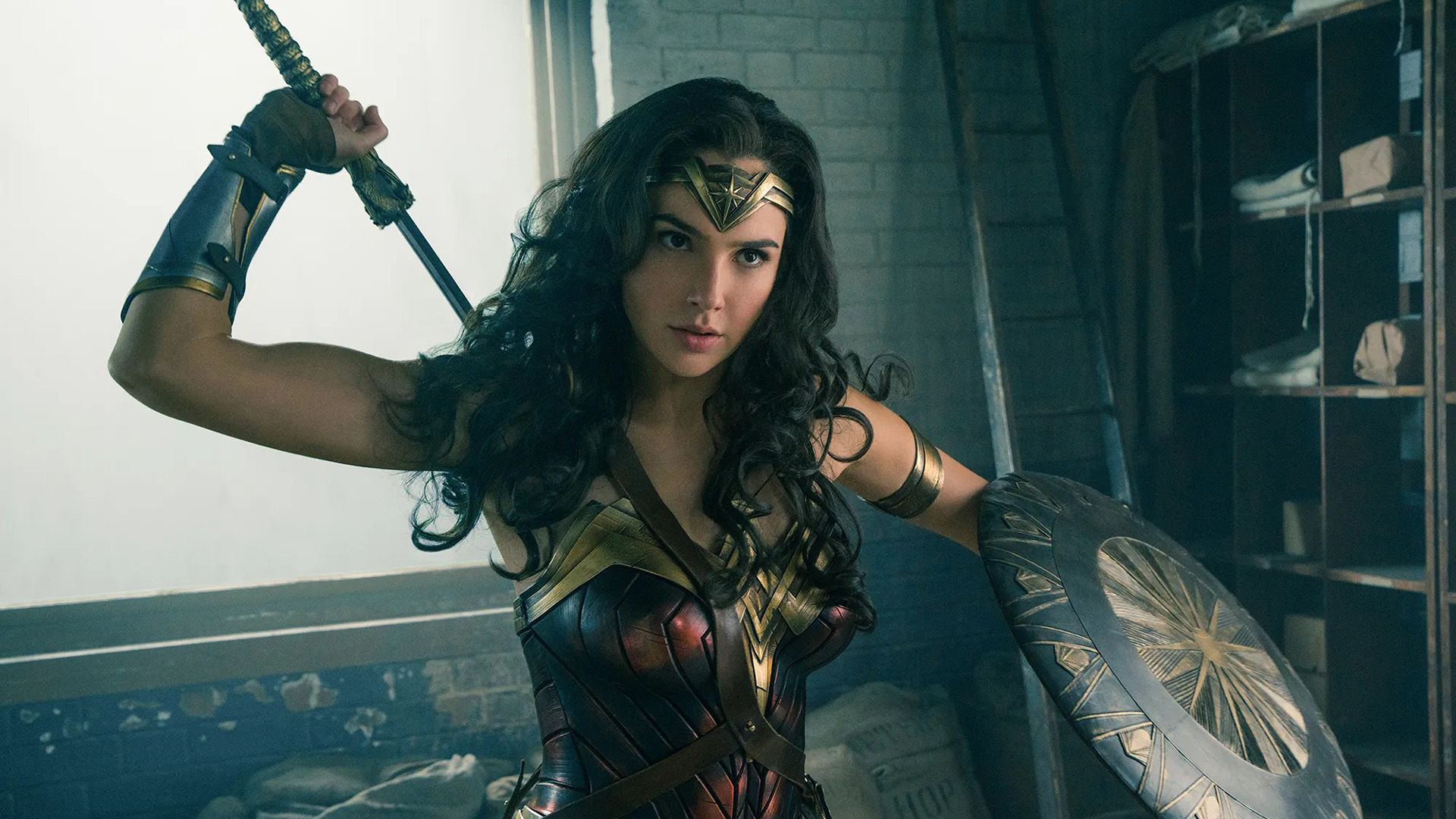 Gal Gadot come Wonder Woman: in armatura, tiene uno scudo con la mano sinistra e tira fuori una spada da dietro la schiena con la mano destra