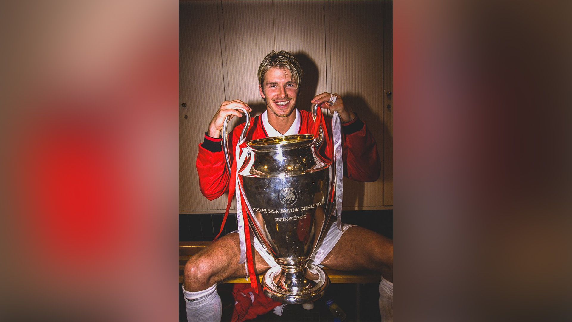 Il giovane David Beckham seduto sulla panchina dello spogliatoio sportivo con la Coppa UEFA