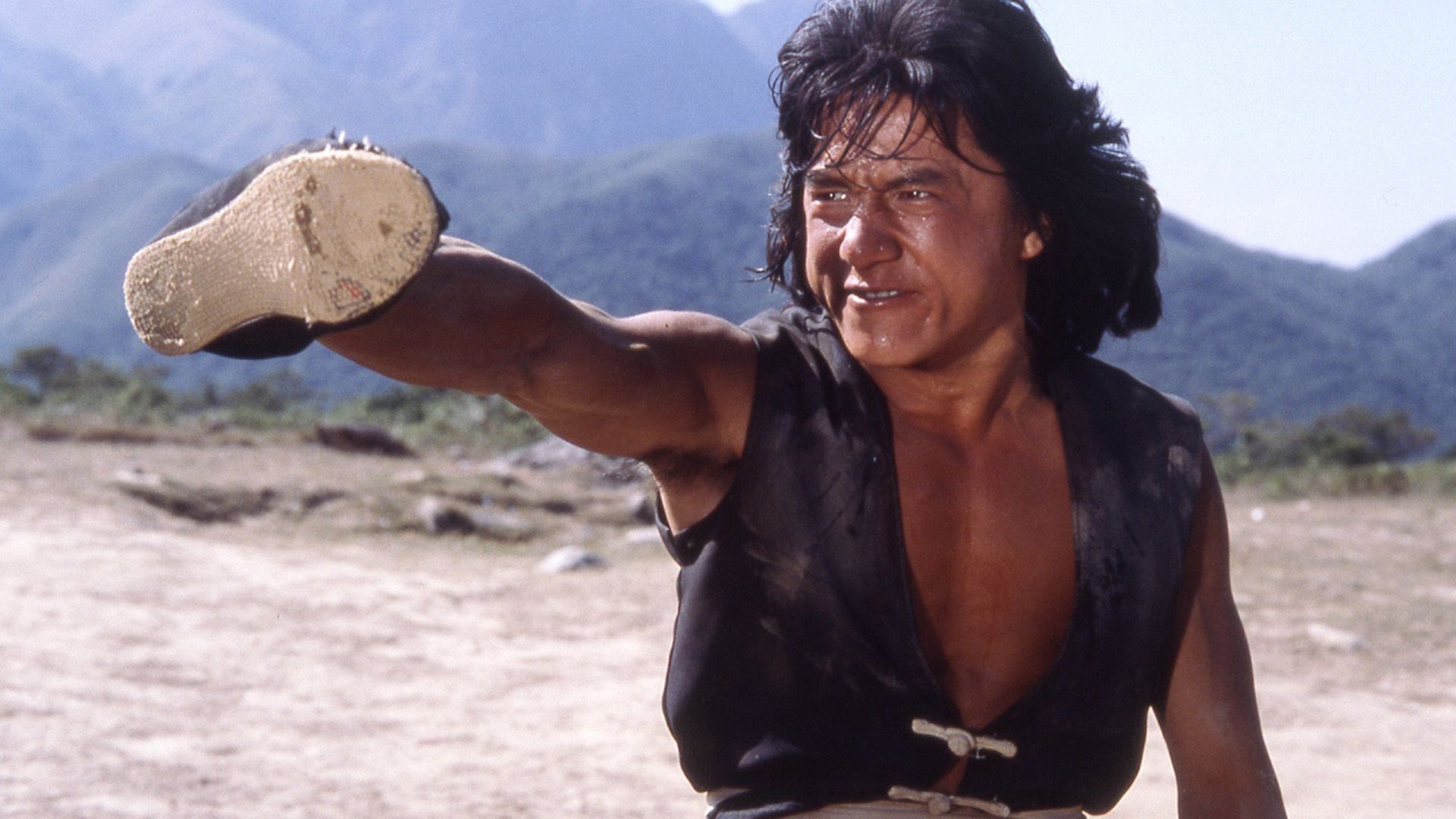 Giovane Jackie Chan in un gilet nero lancia il braccio in avanti con una scarpa in uno strike