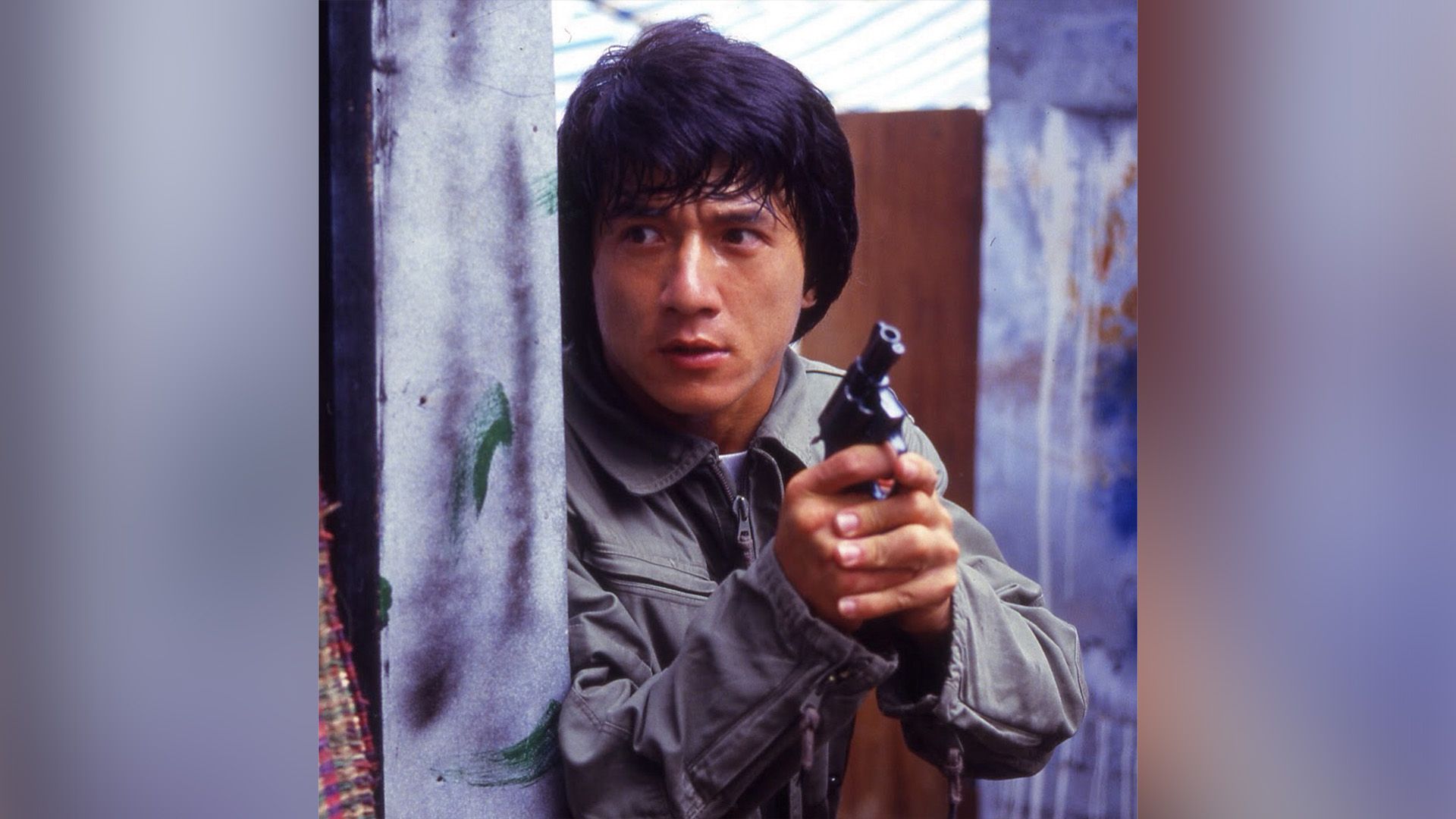 Giovane Jackie Chan con una pistola in mano sbircia dietro l'angolo in una scena del film 'Police Story'