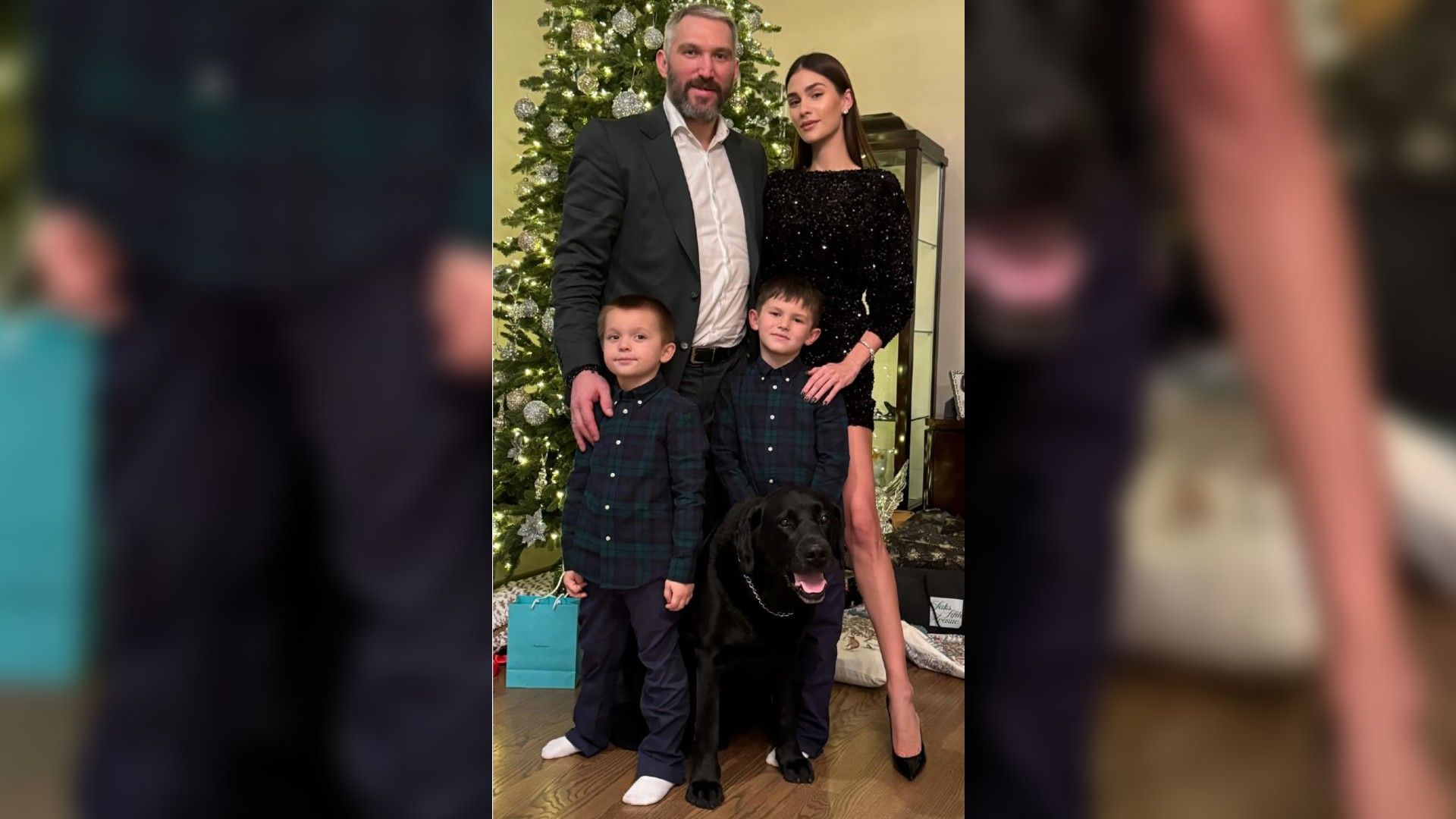 Aleksandr Ovečkin e Anastasia Shubskaya con due ragazzi e un cane nero posano accanto all'albero di Capodanno, i genitori sono vestiti a festa