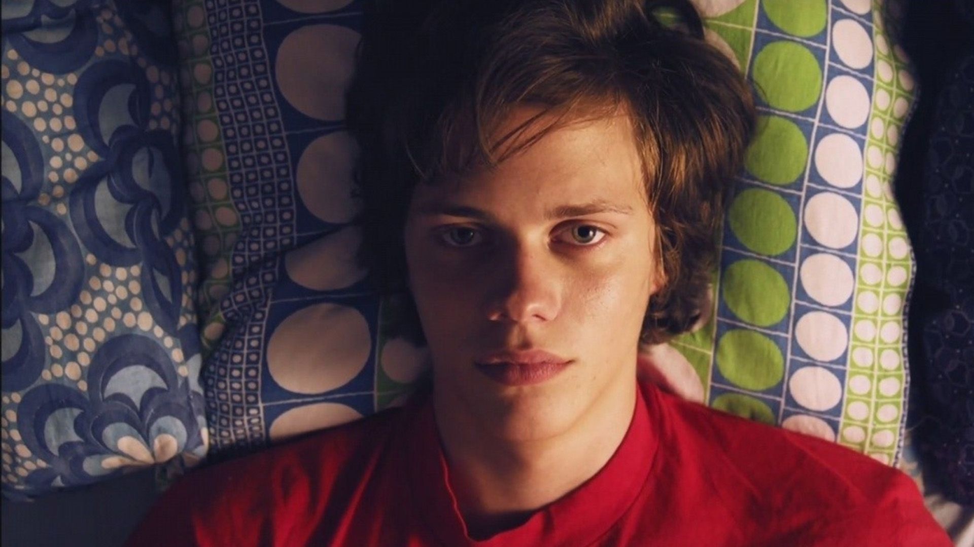 Giovane Bill Skarsgård in una maglietta rossa sdraiato sul letto