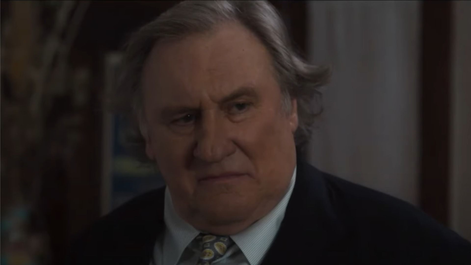 L'attore Gérard Depardieu in un abito classico guarda di lato contro uno sfondo sfocato