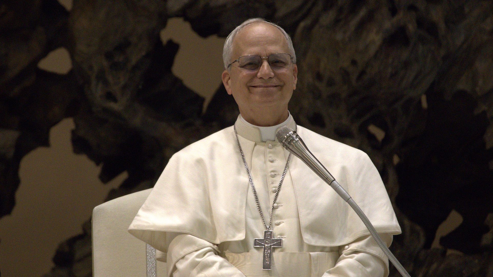 Papa Leone XIV sorridente in abiti bianchi su uno sfondo scuro