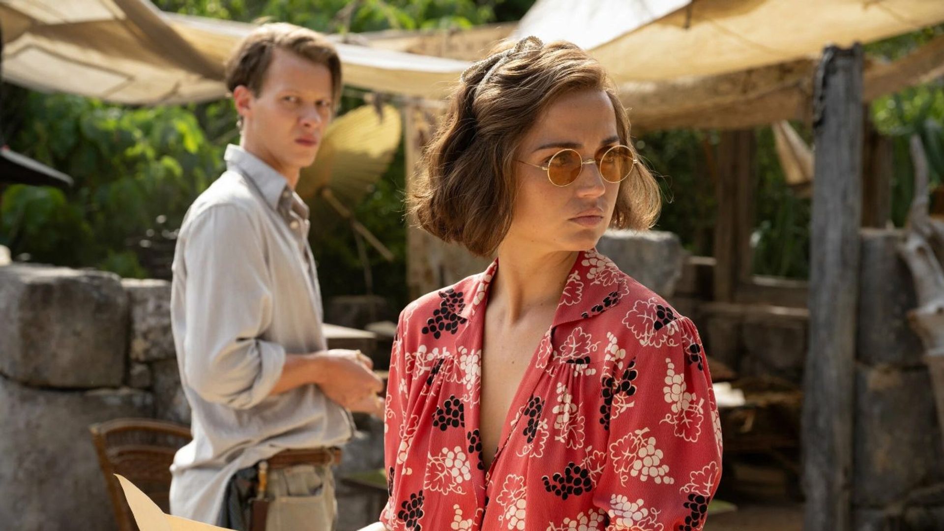 Ana de Armas in una camicetta rossa stampata e occhiali da sole tiene una mappa, in piedi accanto a un uomo in una camicia chiara, la scena ambientata tra rovine archeologiche