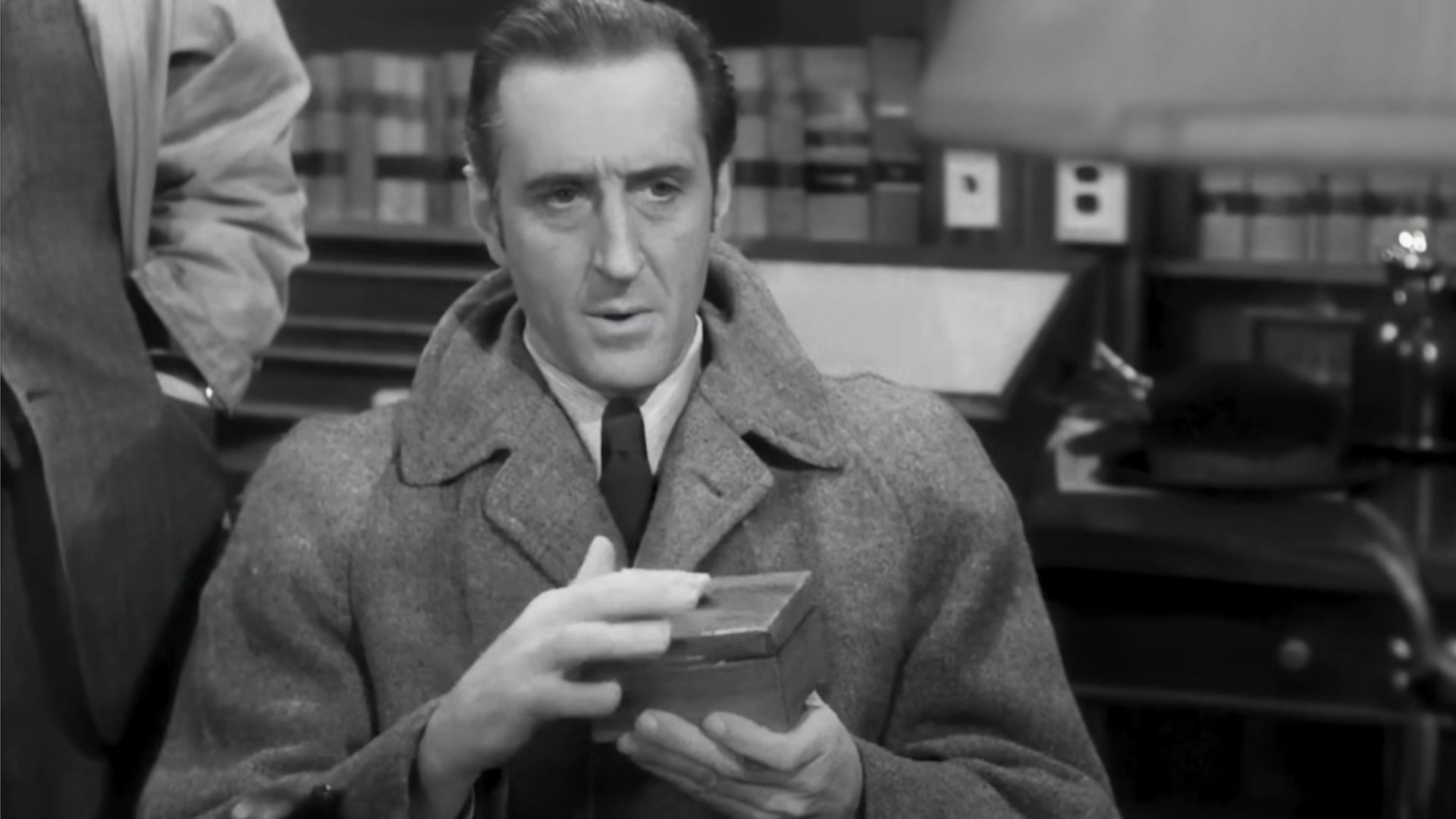 L'attore Basil Rathbone nei panni di Sherlock Holmes tiene una scatola in mano e guarda in basso